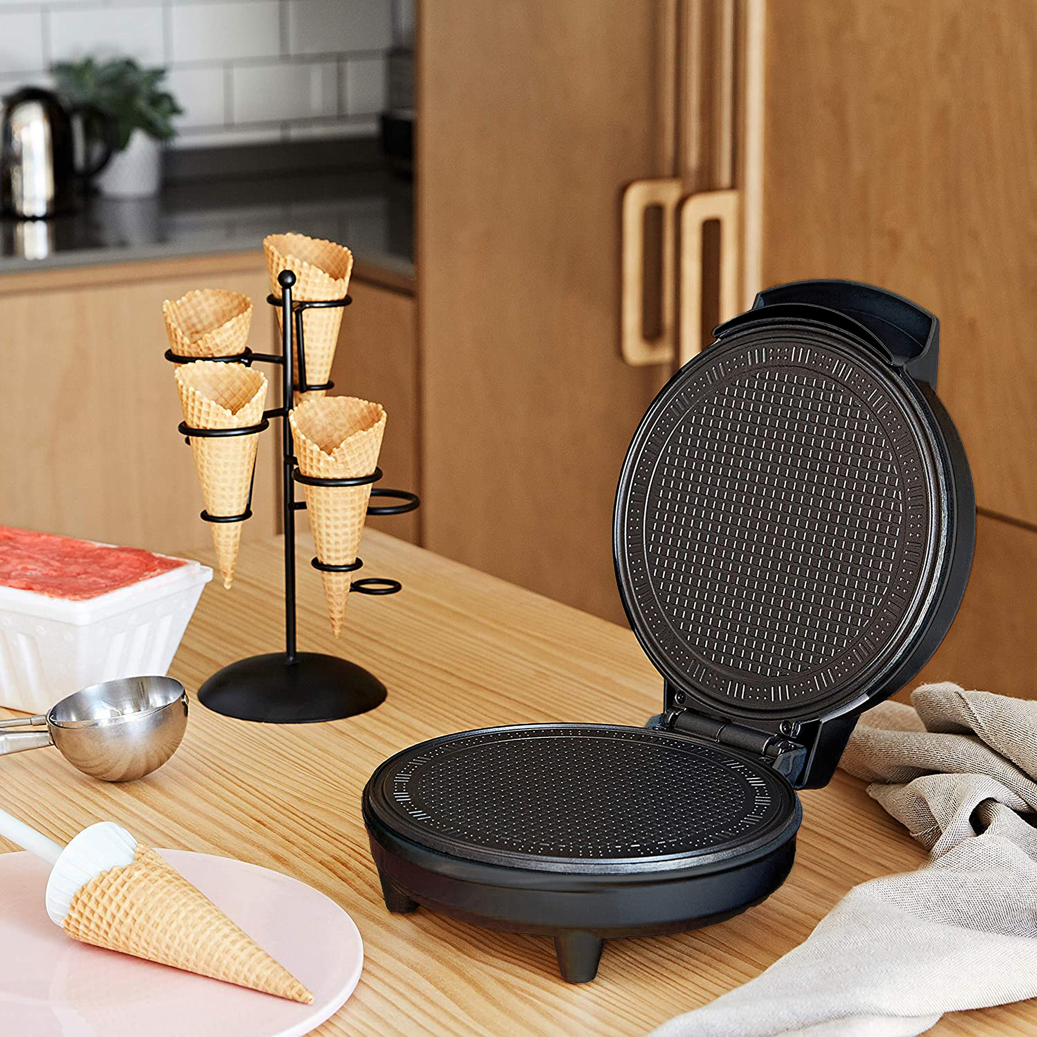 Waffle maker with waffle cones on a rack. Other items on table.