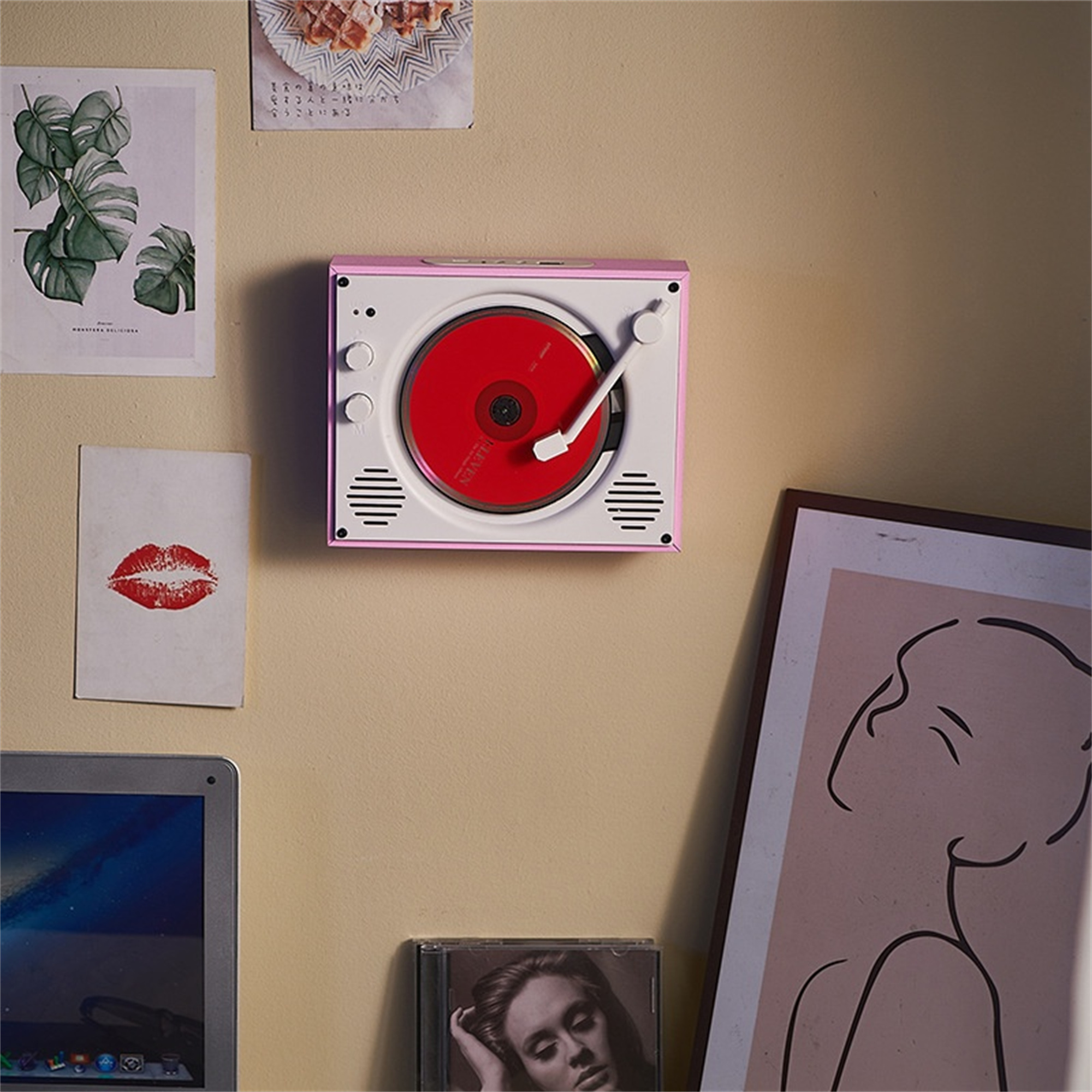 Rosa-weißer Retro-Plattenspieler an einer Wand mit Kunst und einer CD. Eine rote Schallplatte spielt.
