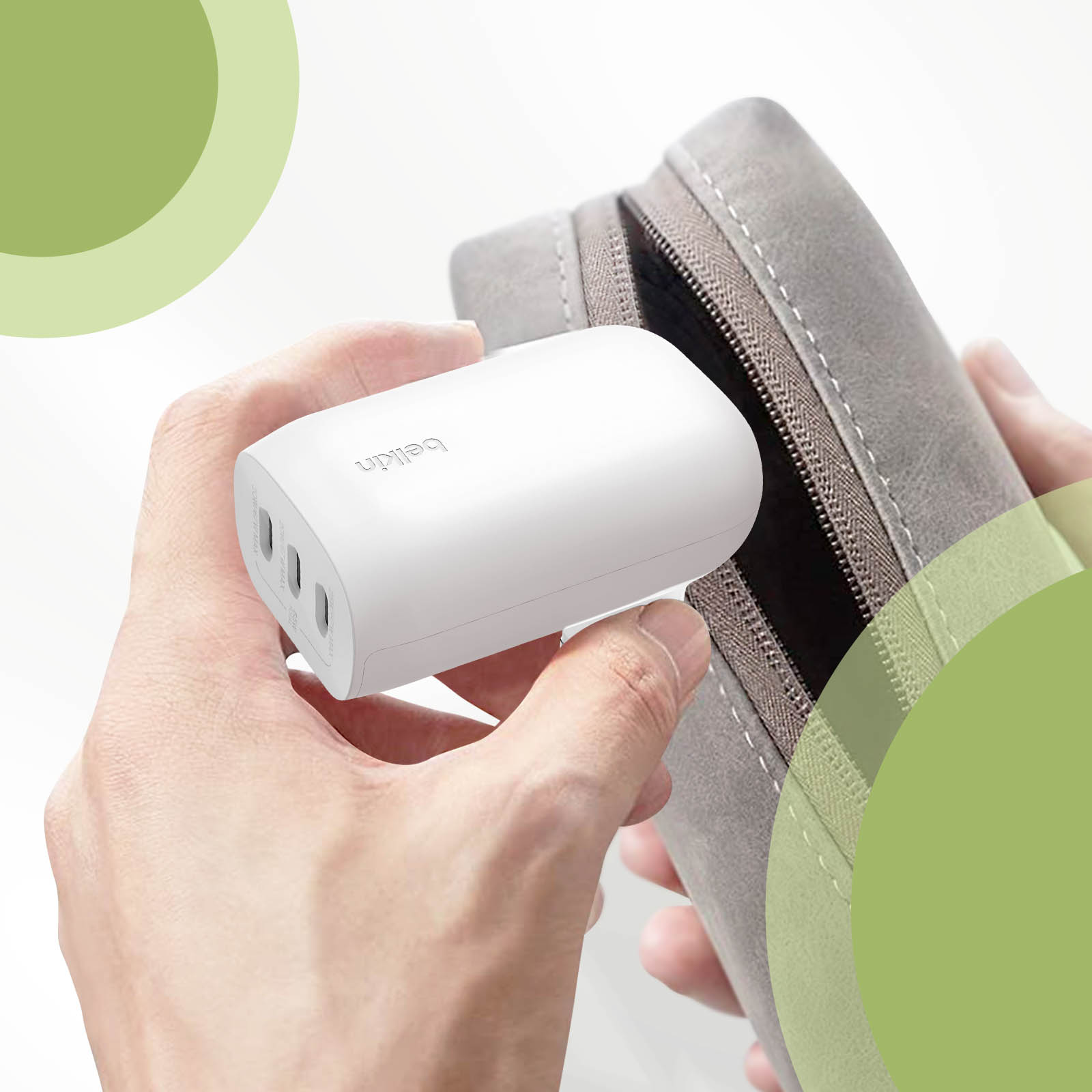 Manos sosteniendo un cargador Belkin blanco y colocándolo en un estuche de viaje gris.