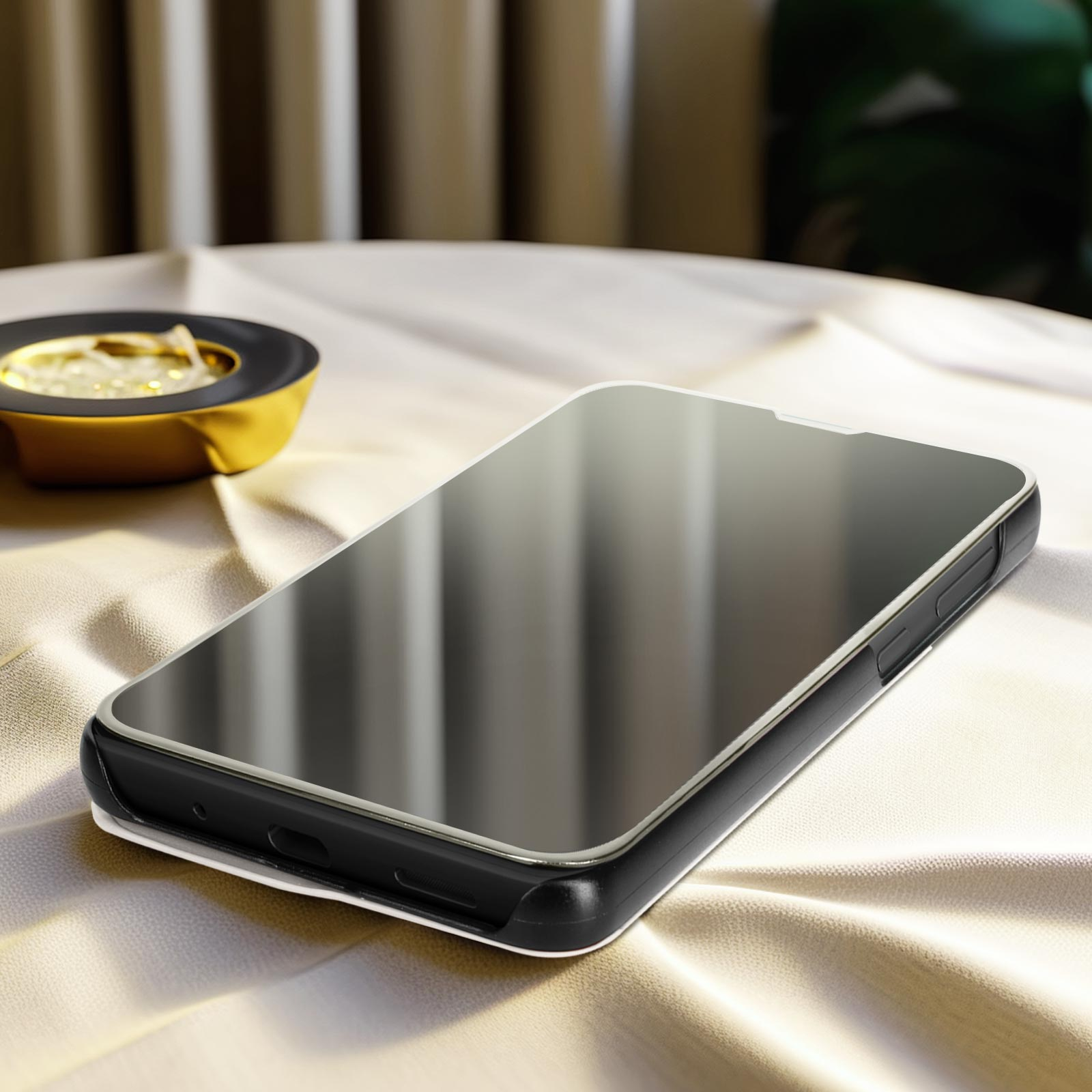 Smartphone su un tavolo con una protezione schermo riflettente, una custodia nera e un posacenere dorato.