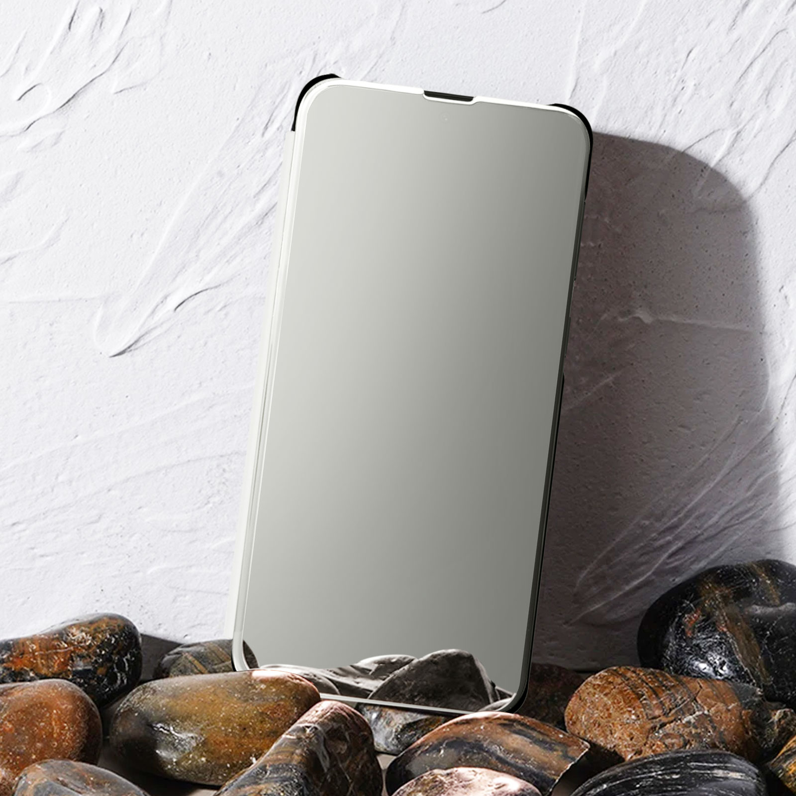 Uno smartphone con display a specchio, appoggiato su pietre contro un muro bianco strutturato.