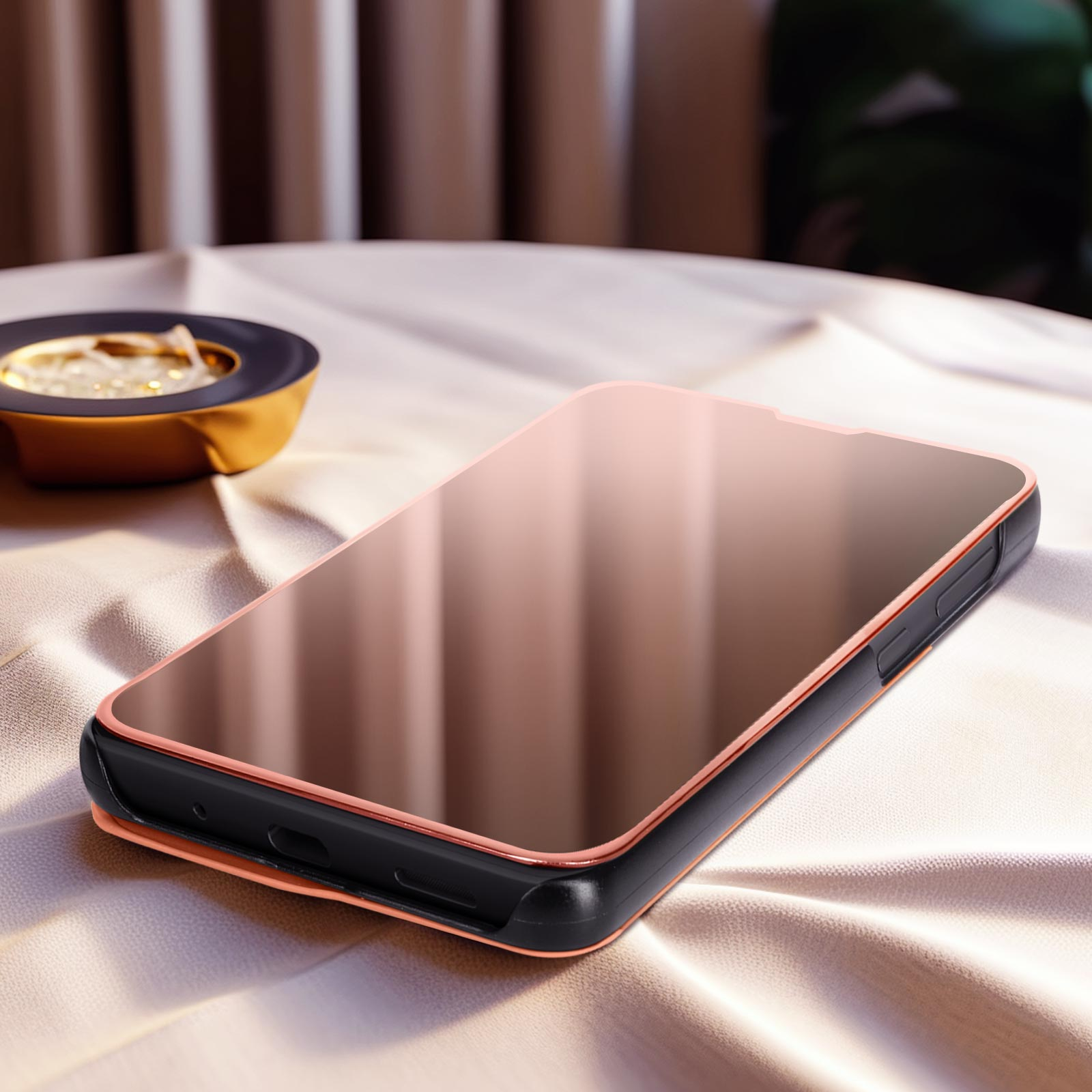 Un telefono con cornice oro rosa su una tovaglia beige, con una piccola ciotola dorata sullo sfondo.