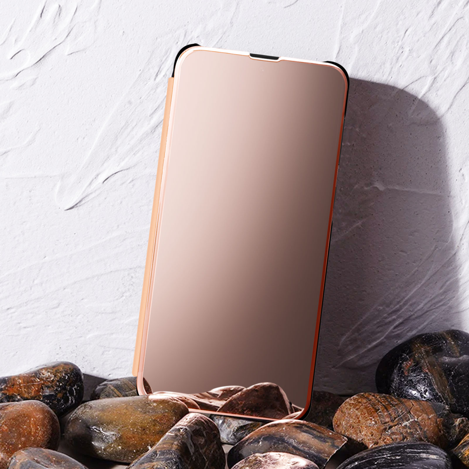 Una custodia per telefono color oro rosa con un telefono all'interno, appoggiata su rocce contro uno sfondo bianco strutturato.