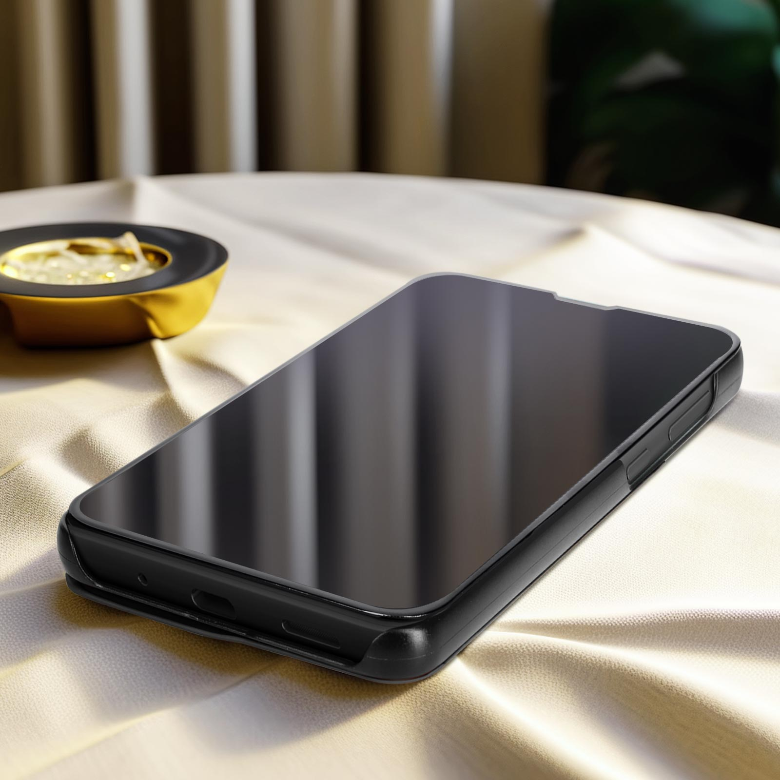 Telefono nero su un tavolo. Ha una protezione per lo schermo. Sfondo: un tessuto con pieghe morbide.
