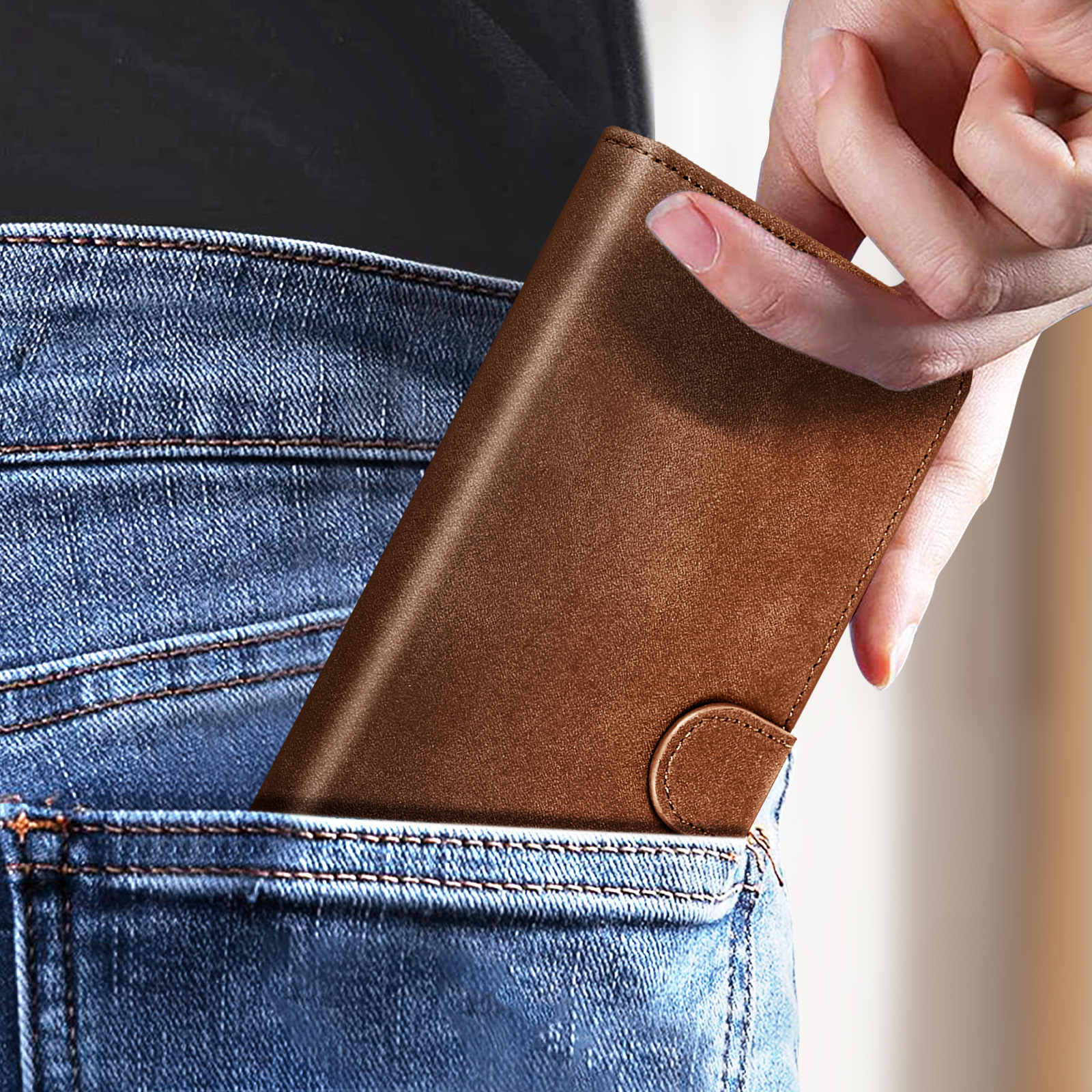 Eine Hand steckt eine braune Lederbrieftasche in eine Jeans-Tasche. Die Brieftasche ist geschlossen.