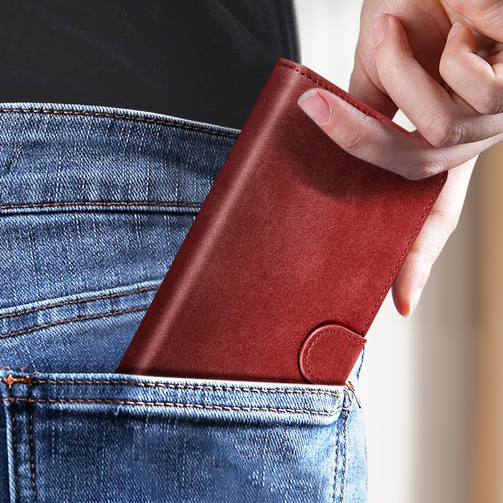Una mano metiendo una cartera roja en un bolsillo de un vaquero. La cartera está cerrada.