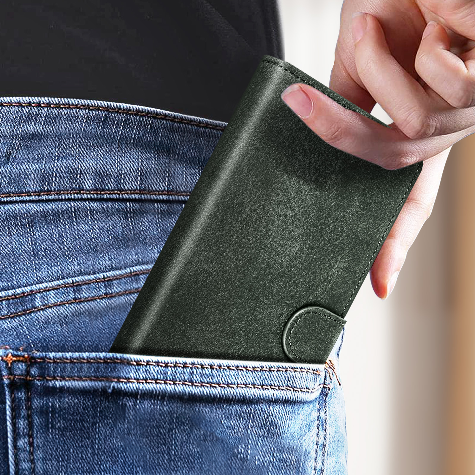 Hand, die eine dunkelgrüne Geldbörse in eine Jeans-Tasche steckt. Heller Hintergrund.