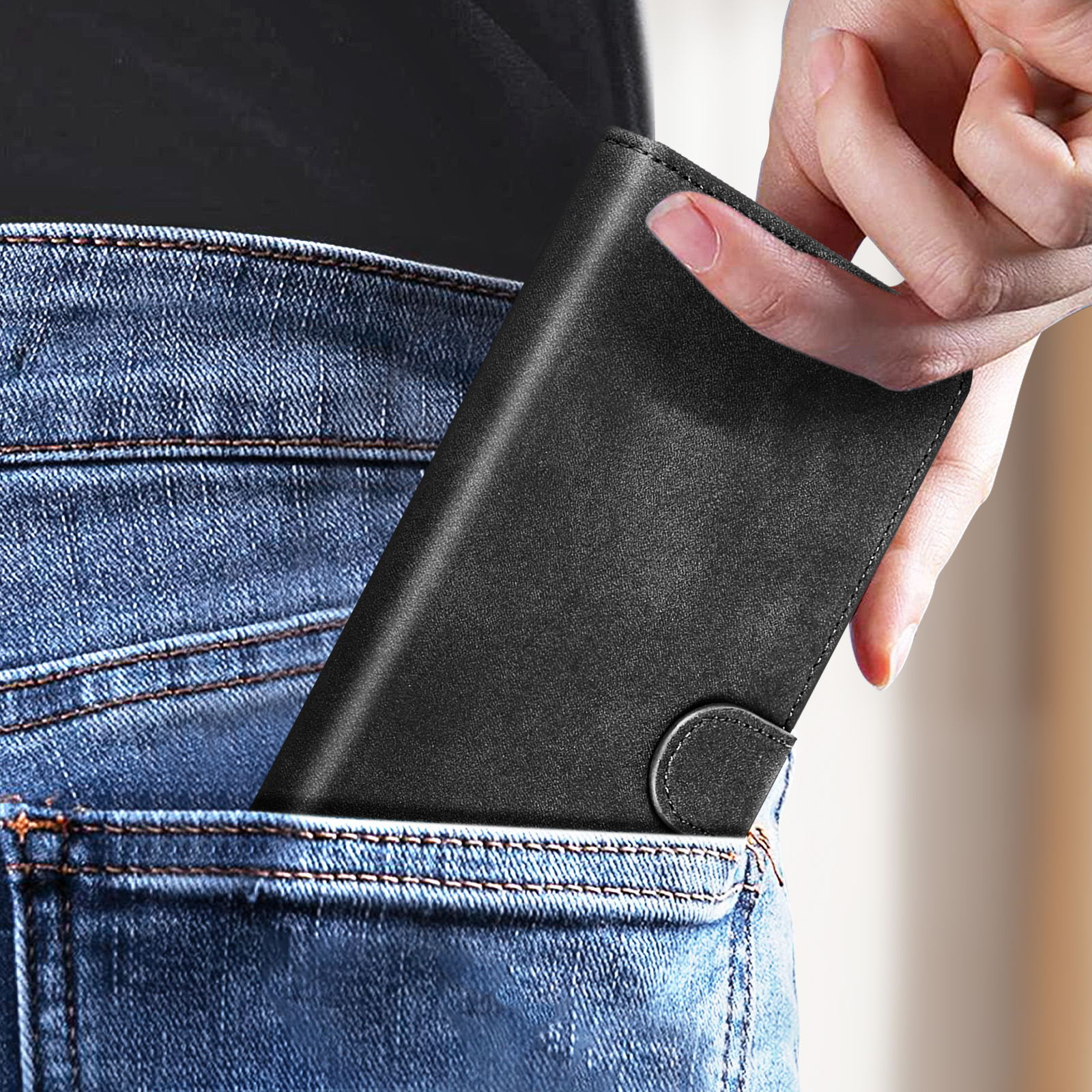 Hand legt schwarze Geldbörse in eine blaue Jeans-Tasche. Die Geldbörse ist aus Leder, mit Knopfverschluss.