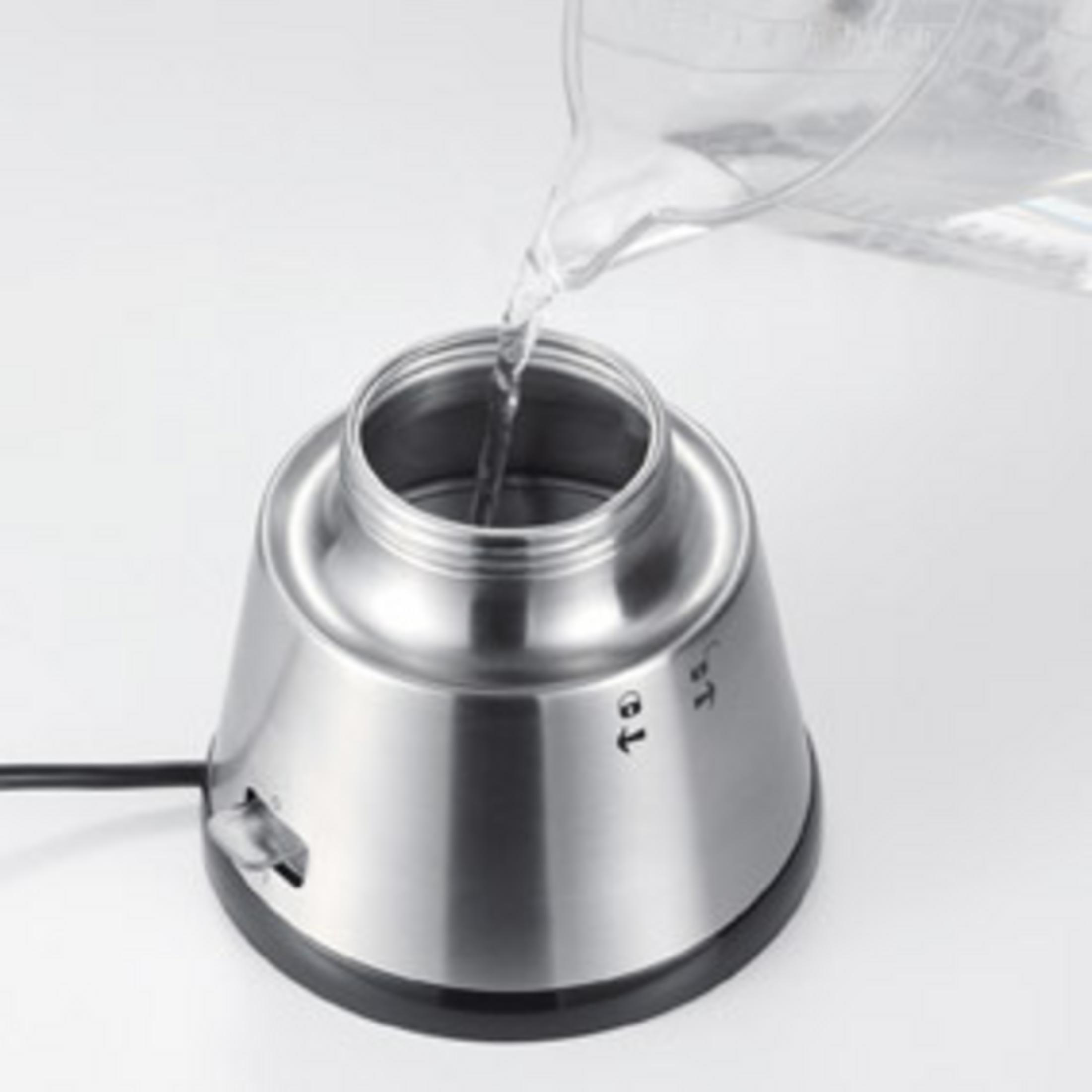 Woda wlewana do czajnika ze stali nierdzewnej. Czajnik stoi na białej powierzchni.