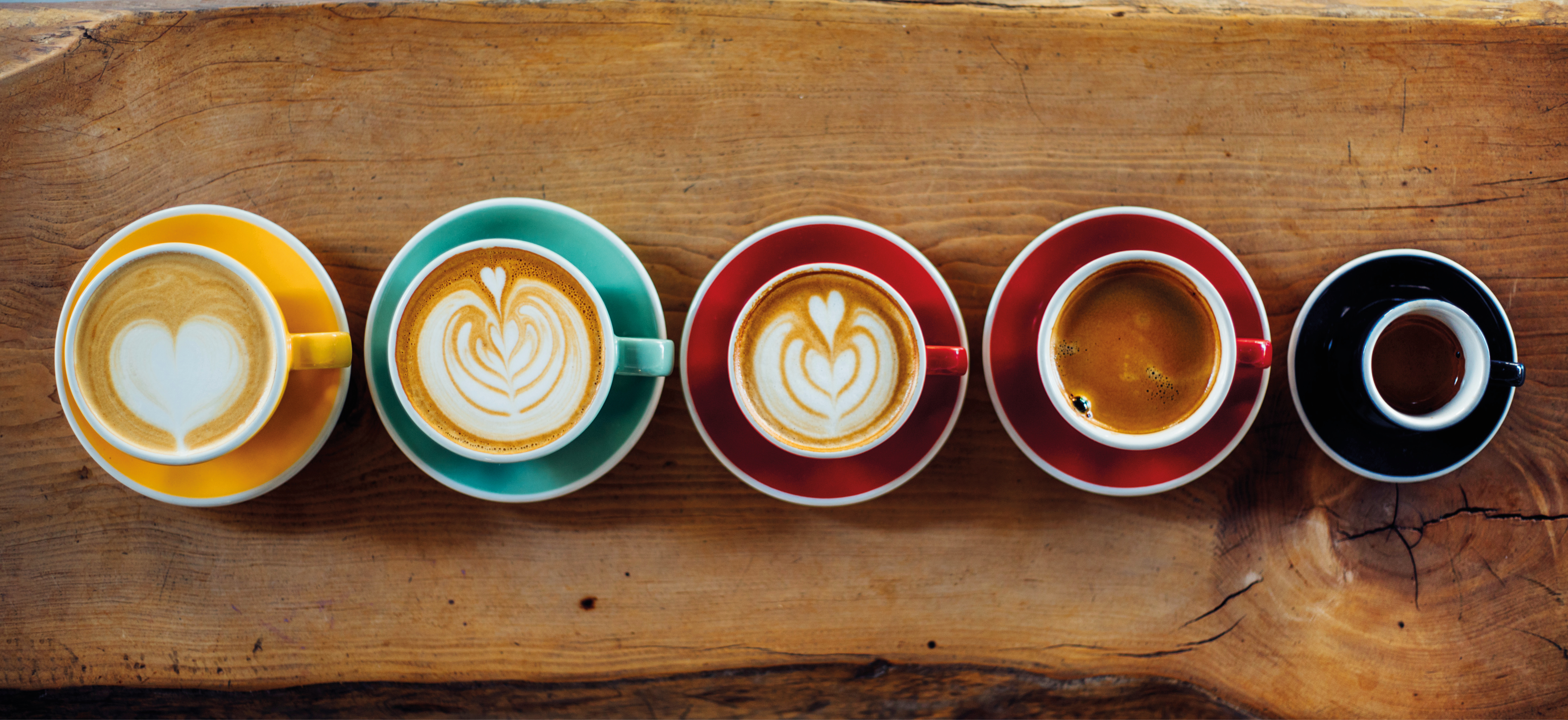 Widok z góry na filiżanki kawy z latte art, ułożone na drewnianej powierzchni.