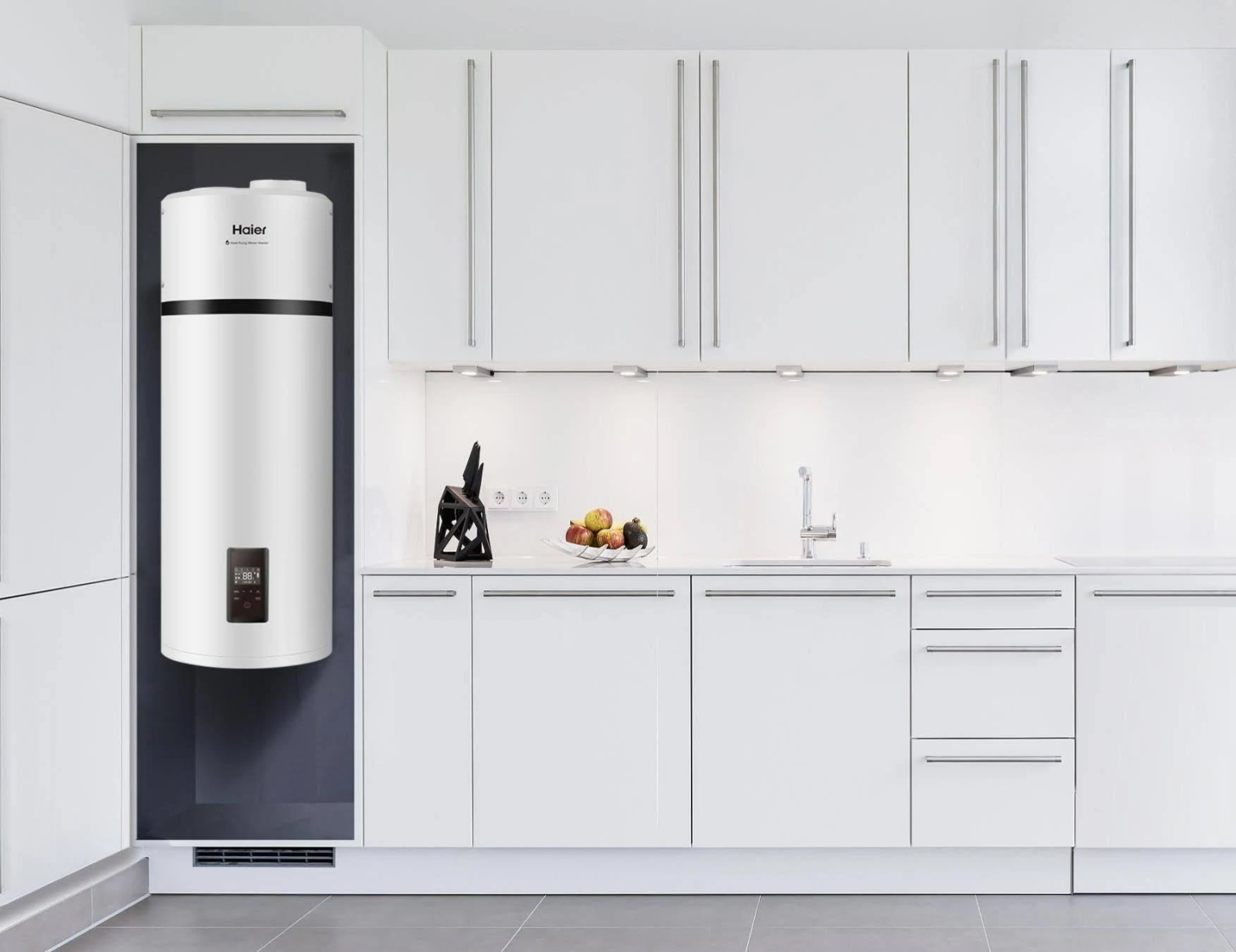 Cocina blanca con gabinetes blancos. Un calentador de agua Haier está montado en la pared. Frutas y utensilios están en el mostrador.