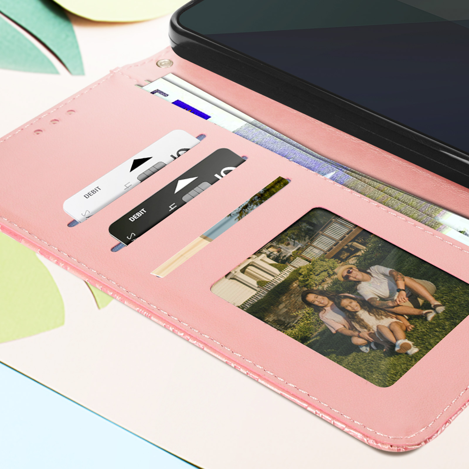 Custodia rosa per telefono con carte e foto di famiglia. Lo sfondo è un motivo a foglie verdi.