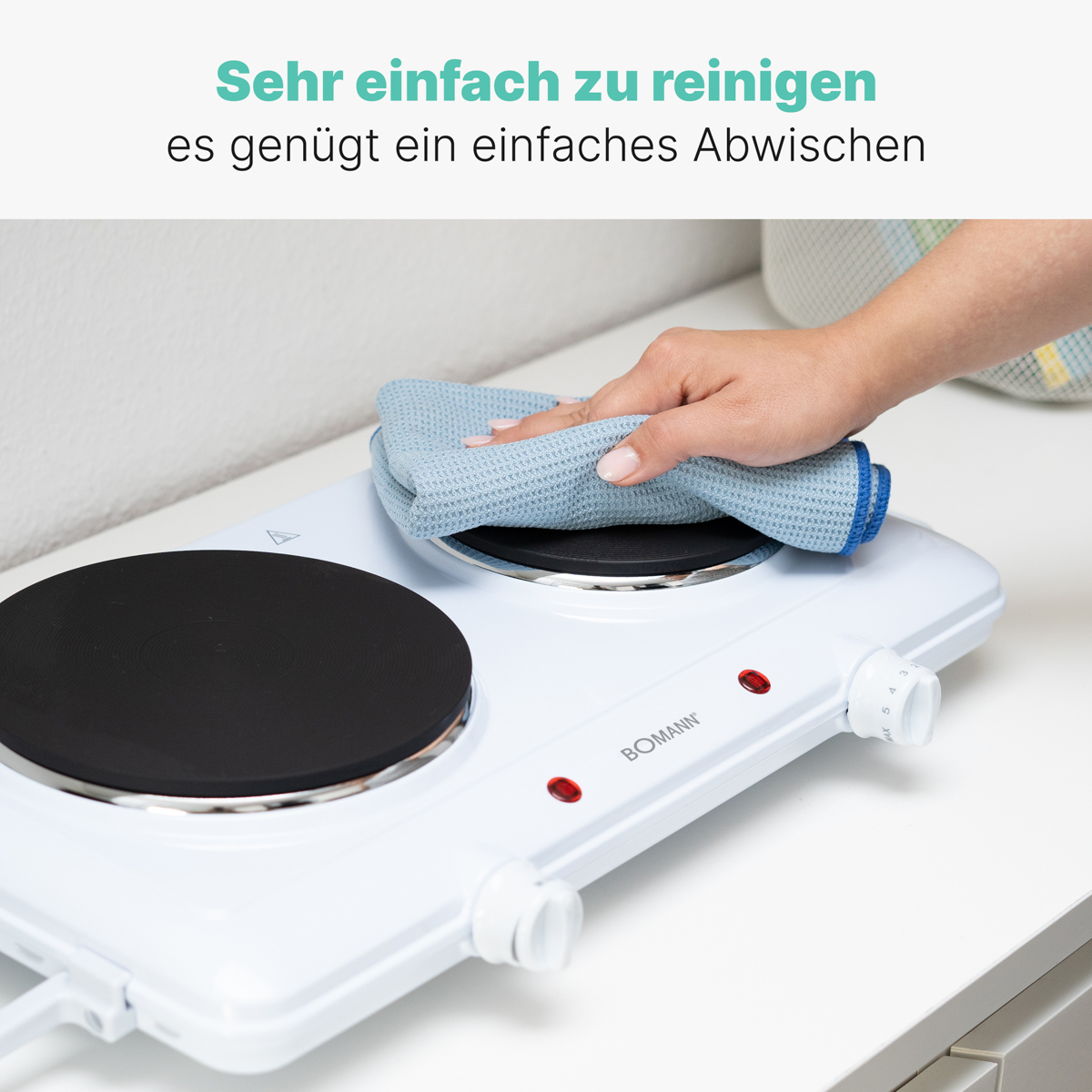 Biała płyta grzewcza czyszczona niebieską szmatką. Tekst po niemiecku powyżej.