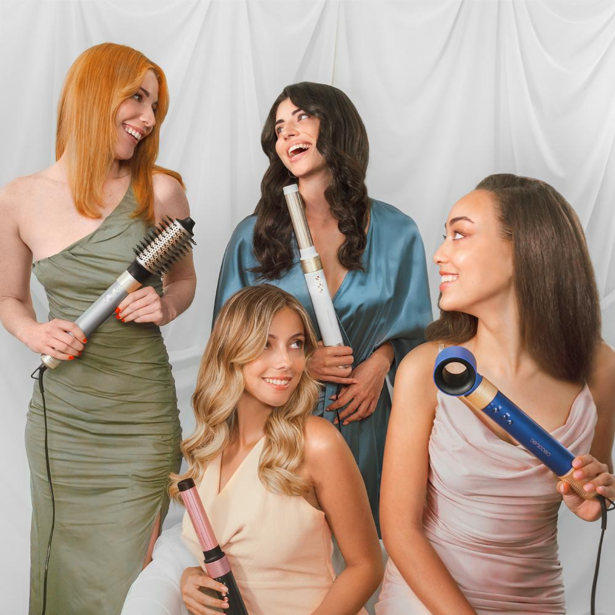 Four women with hair styling tools. One has a curling iron, others have hair stylers.