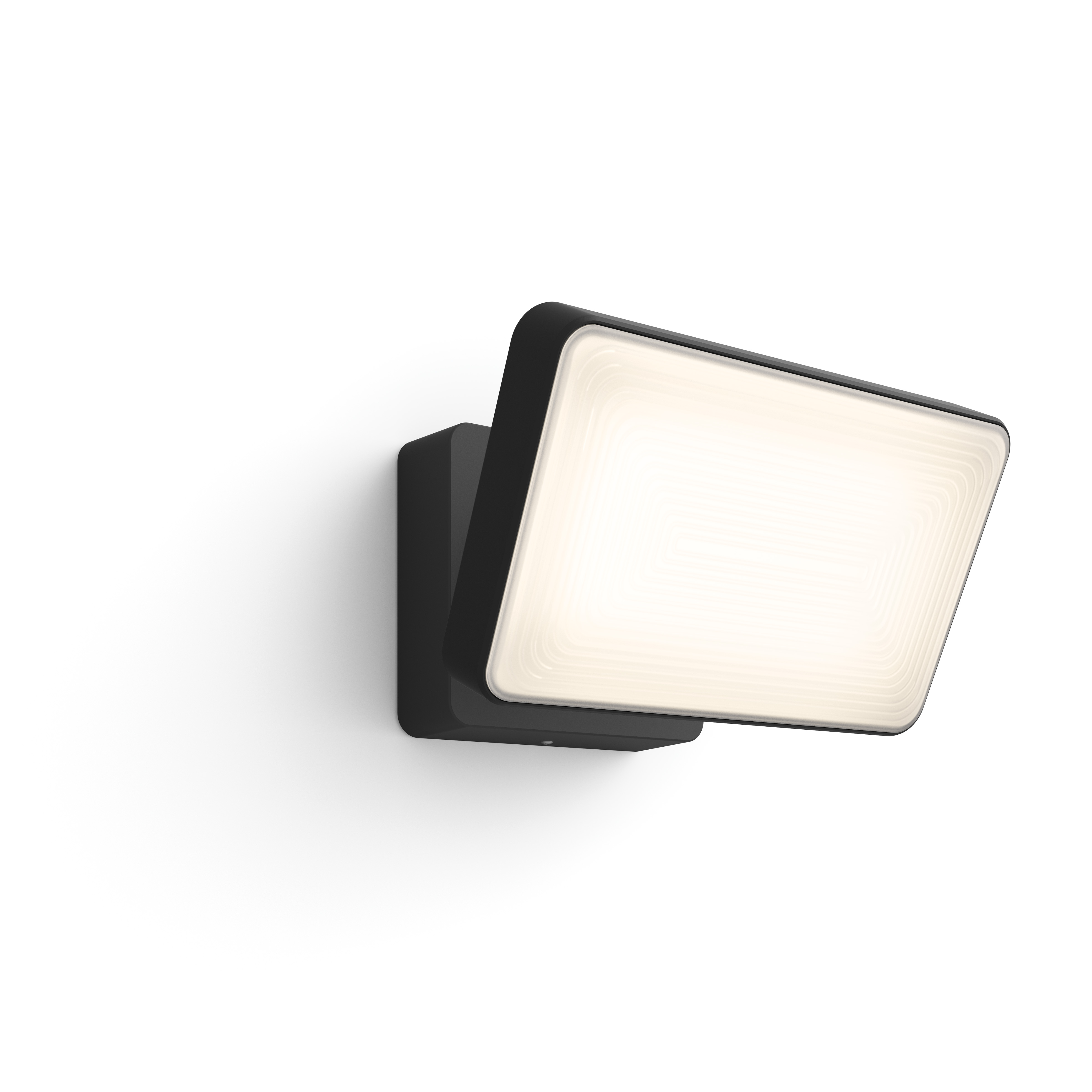 Projecteur extérieur noir monté sur un mur blanc. La lumière est inclinée, émettant une lumière blanche vive.