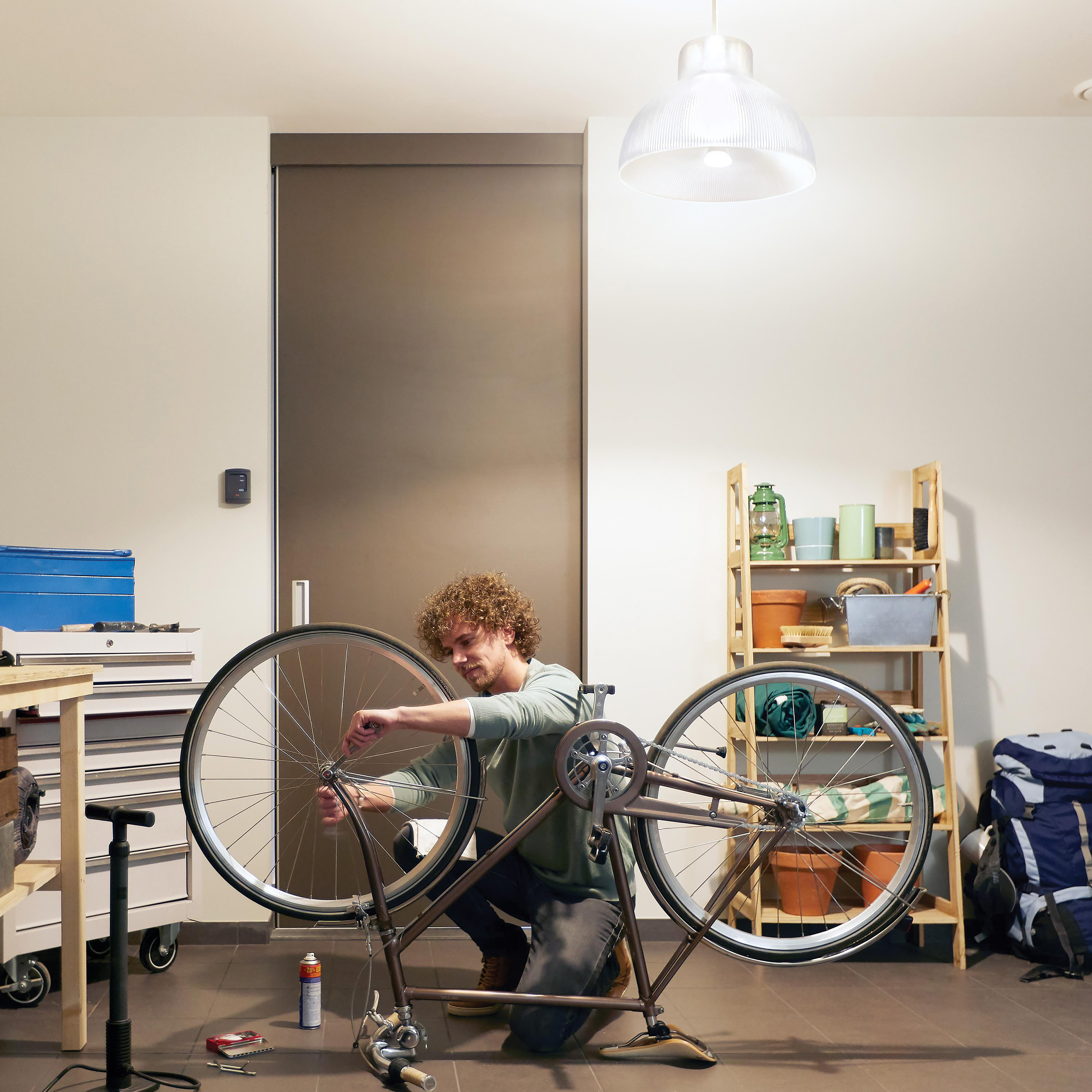 Mężczyzna naprawiający koło roweru w garażu, otoczony narzędziami i sprzętem.