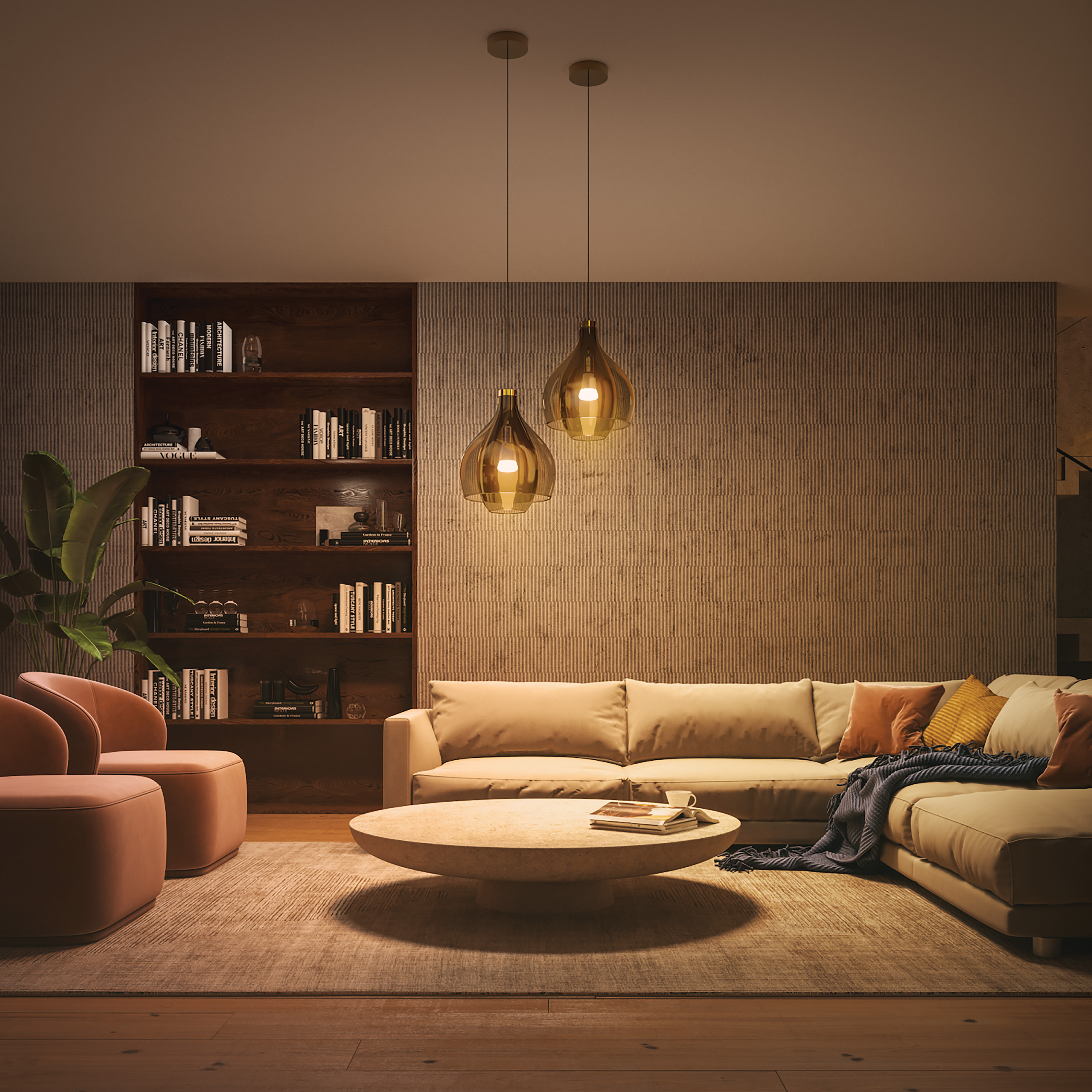 Salón con sofá beige, dos sillones rosas y dos lámparas colgantes. Estanterías en el fondo.