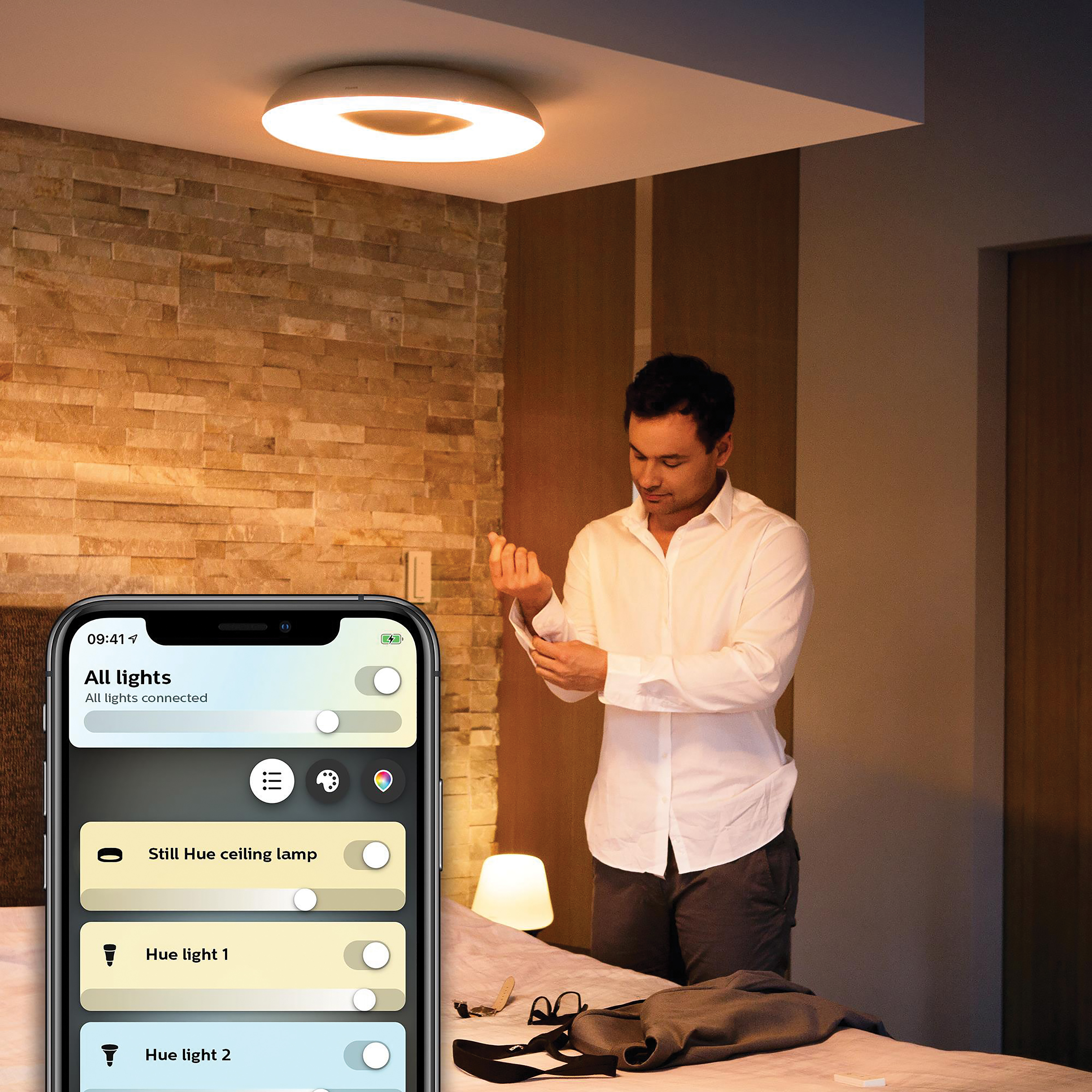 Homme en chemise blanche ajustant manchette, smartphone montrant application, plafonnier.