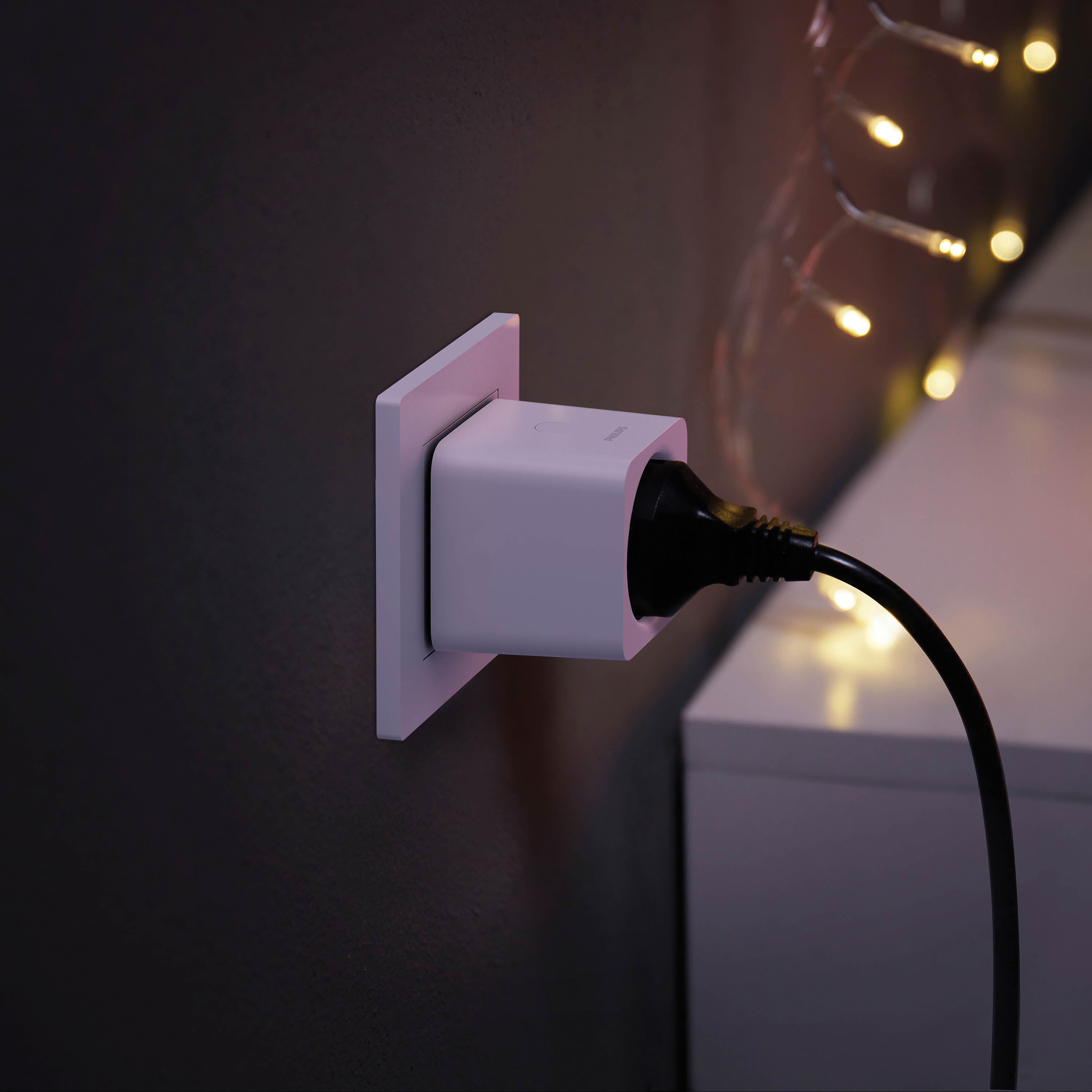 White smart plug inserted into a wall outlet, with a black cable and fairy lights.
