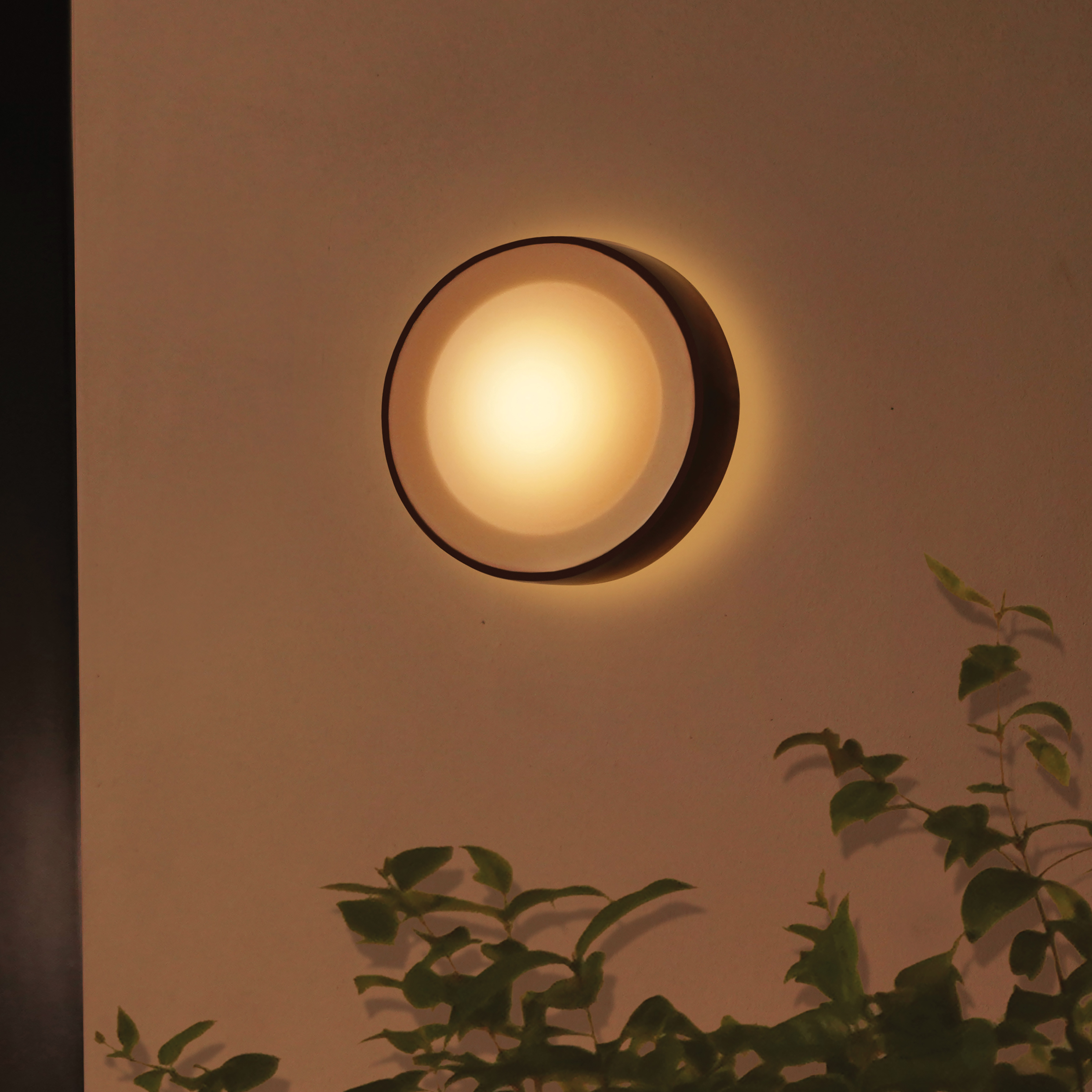 Ronde buitenmuurlamp, met warm licht, op een beige muur.