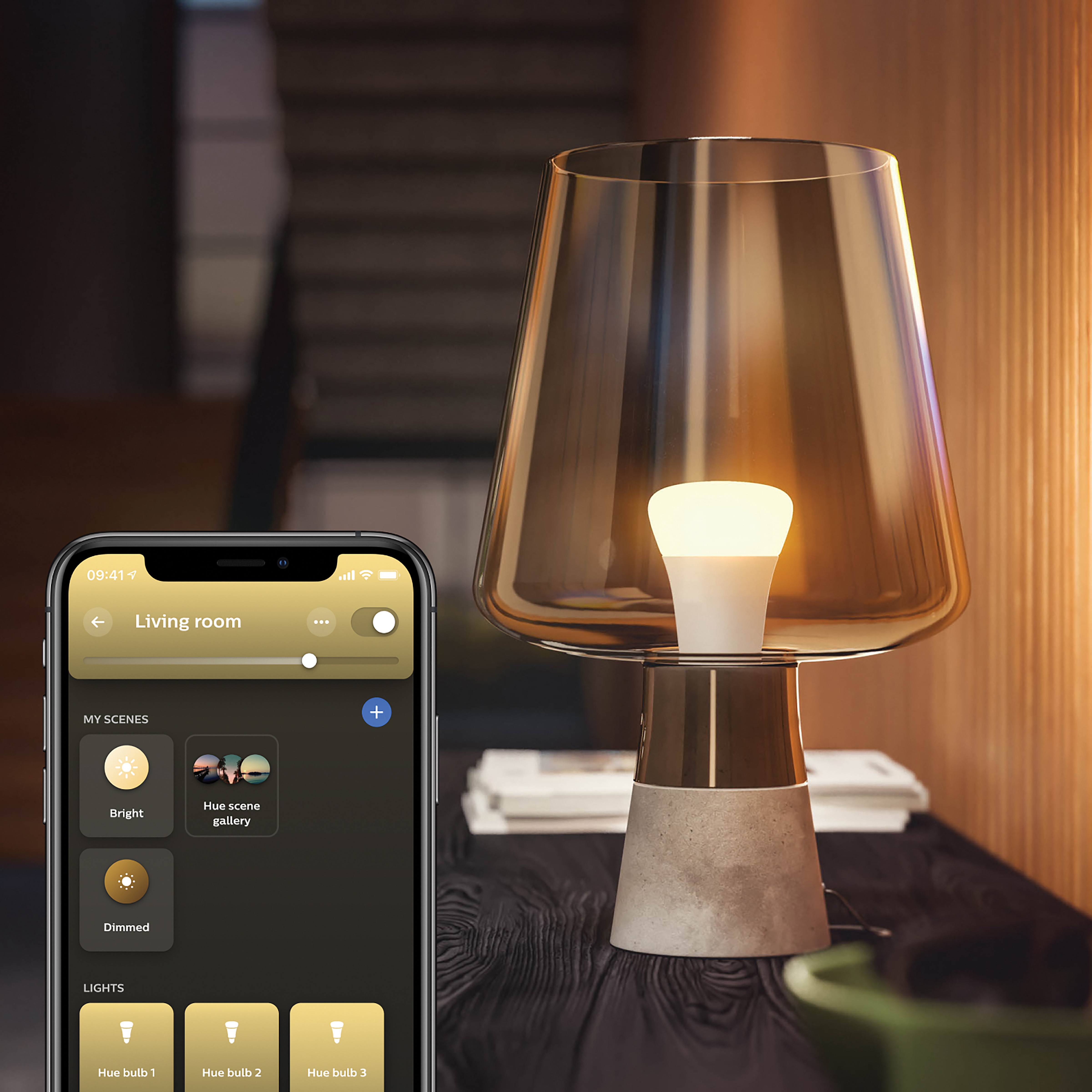 Une lampe intelligente avec un téléphone affichant les options de contrôle. Une lampe est sur une table avec une lumière chaude.