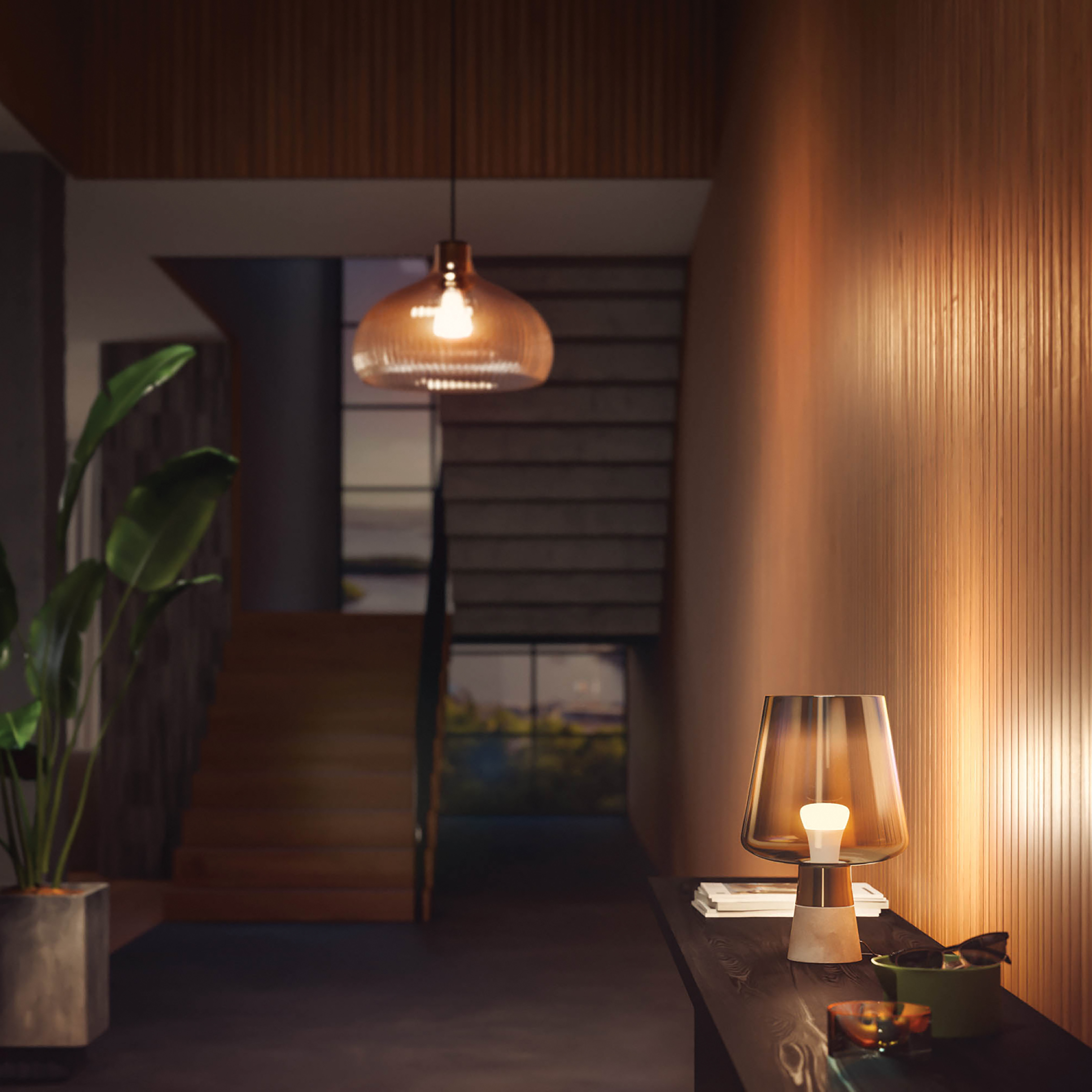 Une lampe sur une table dans un couloir. Il y a un escalier et une plante en arrière-plan.