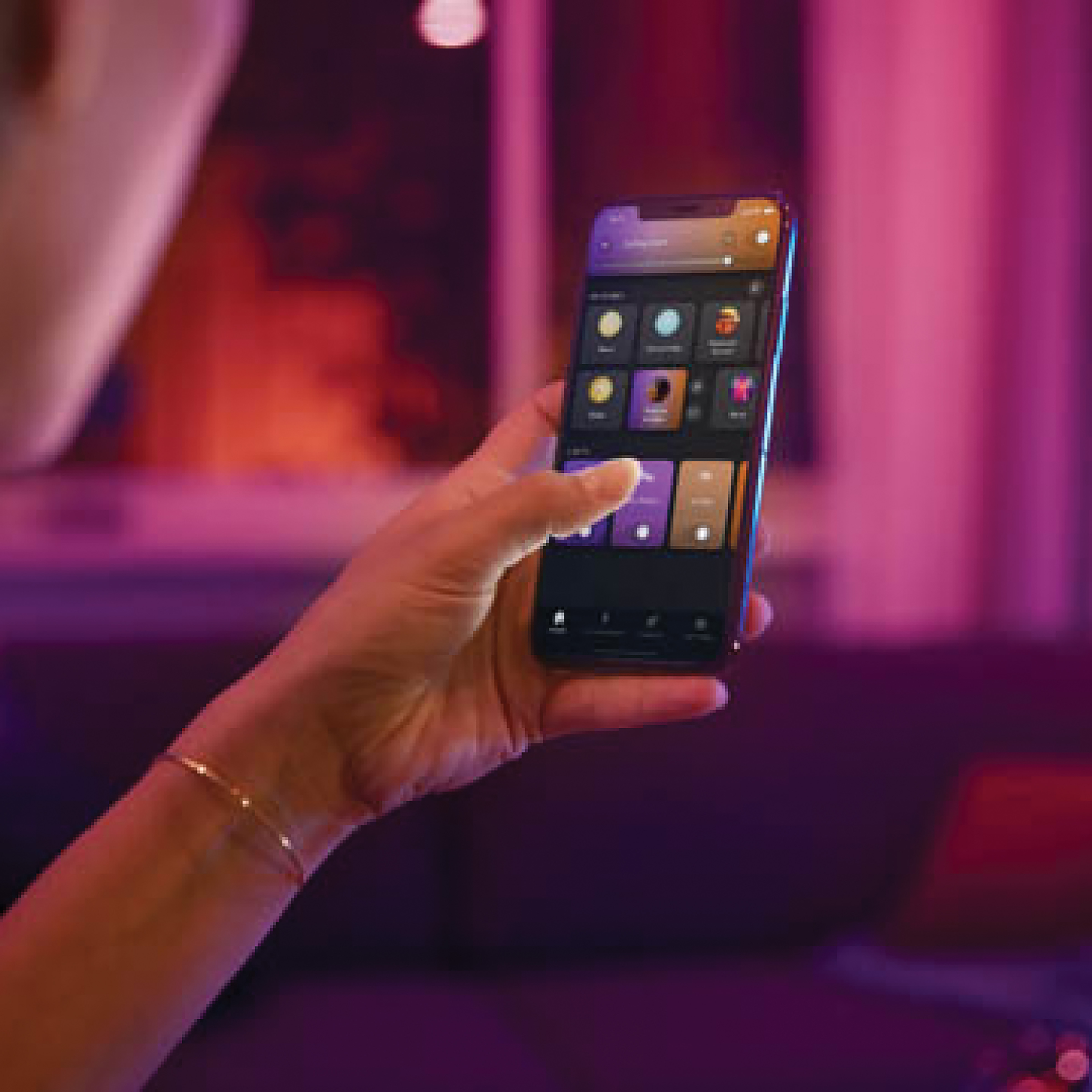 Dłoń trzymająca telefon z interfejsem aplikacji, fioletowe i czerwone światło otoczenia w tle.