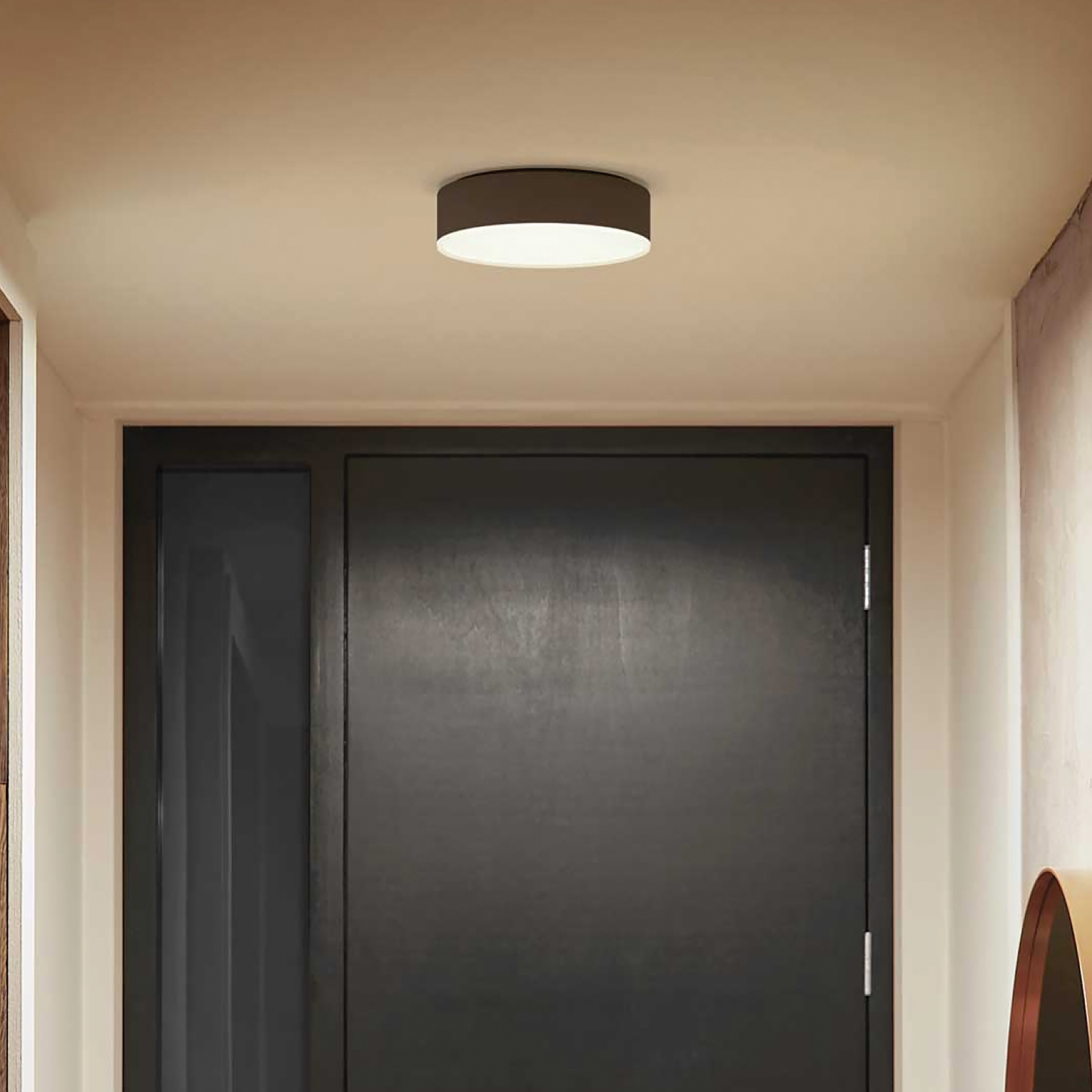 Oprawa oświetleniowa sufitowa, czarna, wyśrodkowana nad ciemnymi drzwiami.