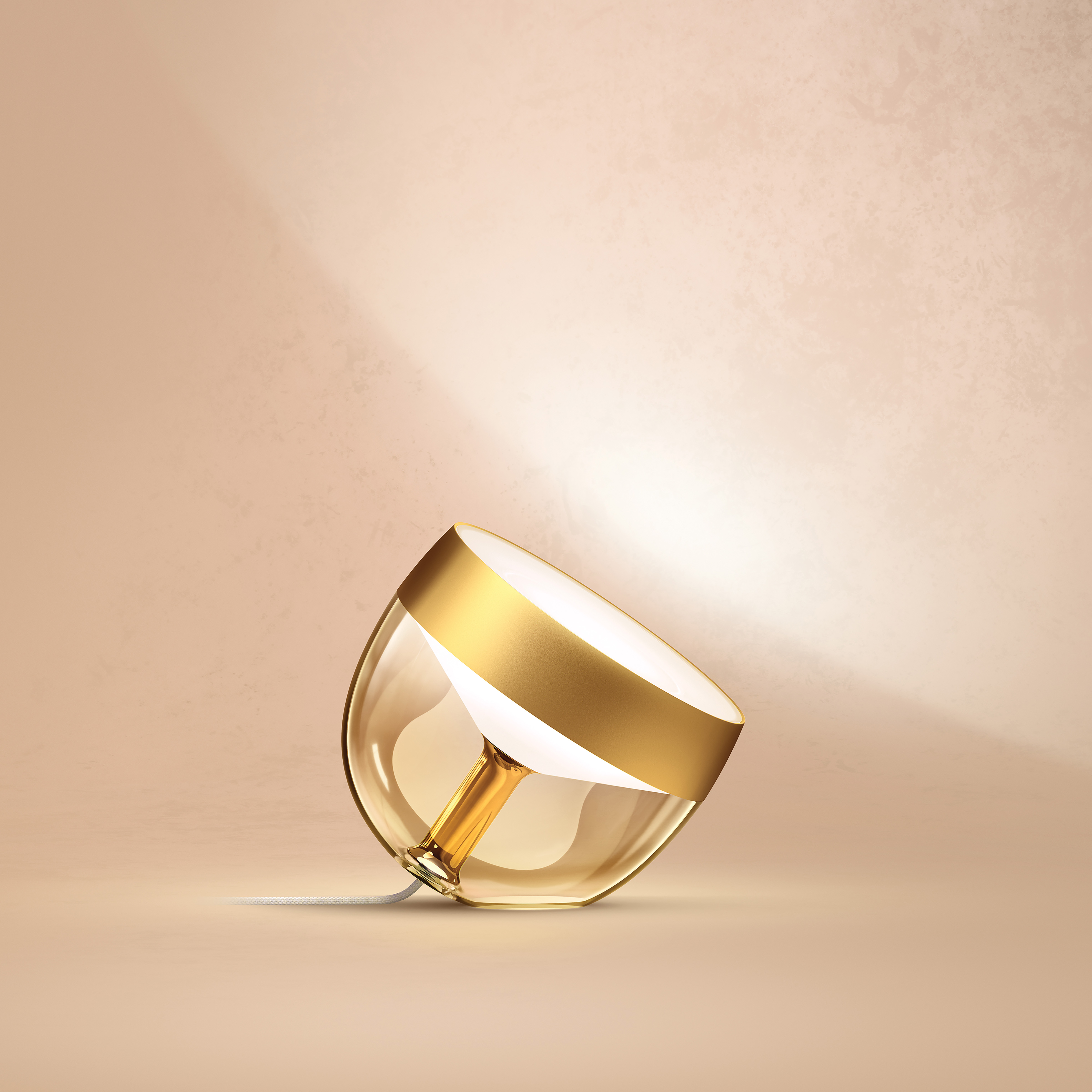 Eine goldene und gläserne Lampe, schräg auf beigem Hintergrund, wirft warmes Licht.