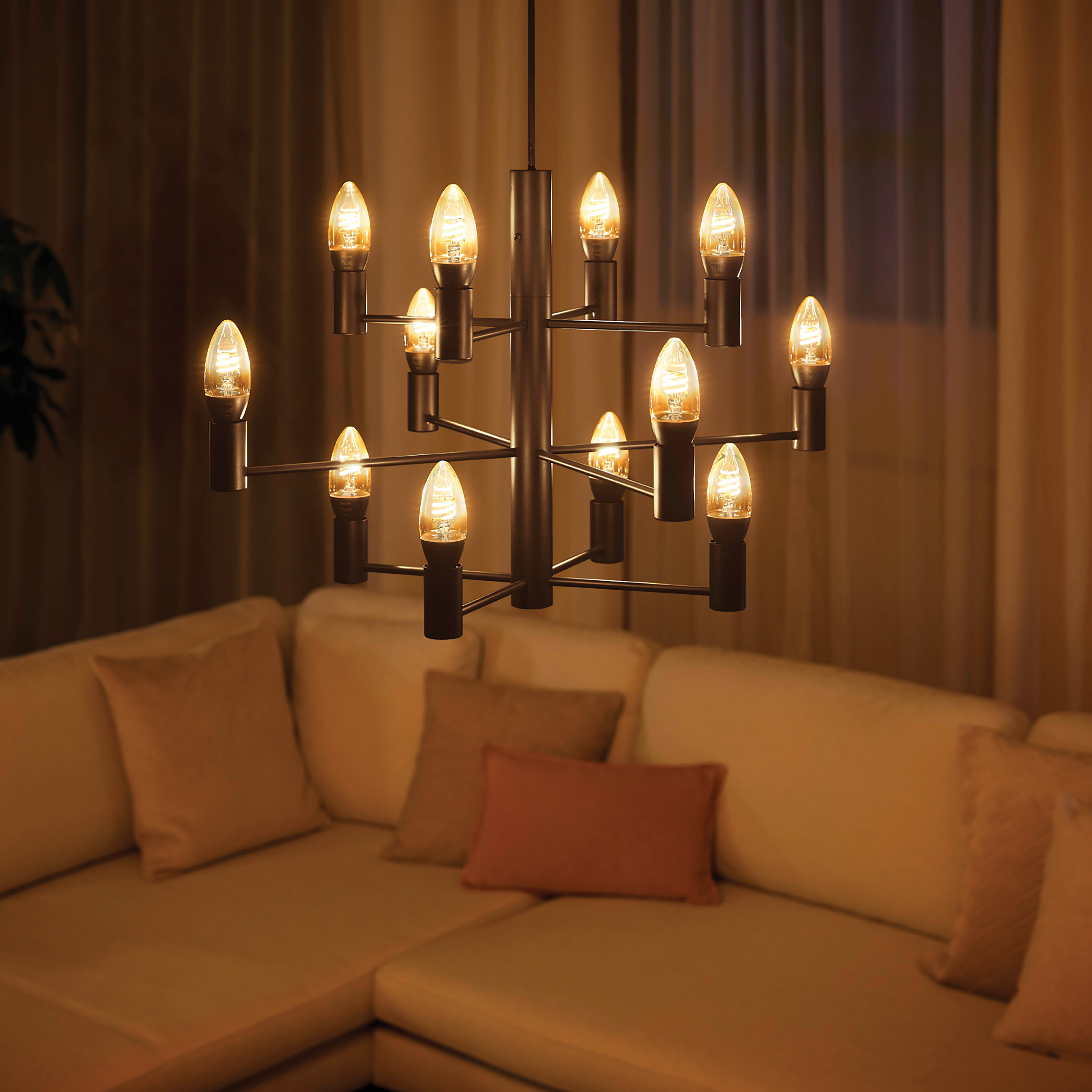 Żyrandol z wieloma żarówkami w stylu Edisona. Beżowa sofa w tle. Ciepłe oświetlenie.