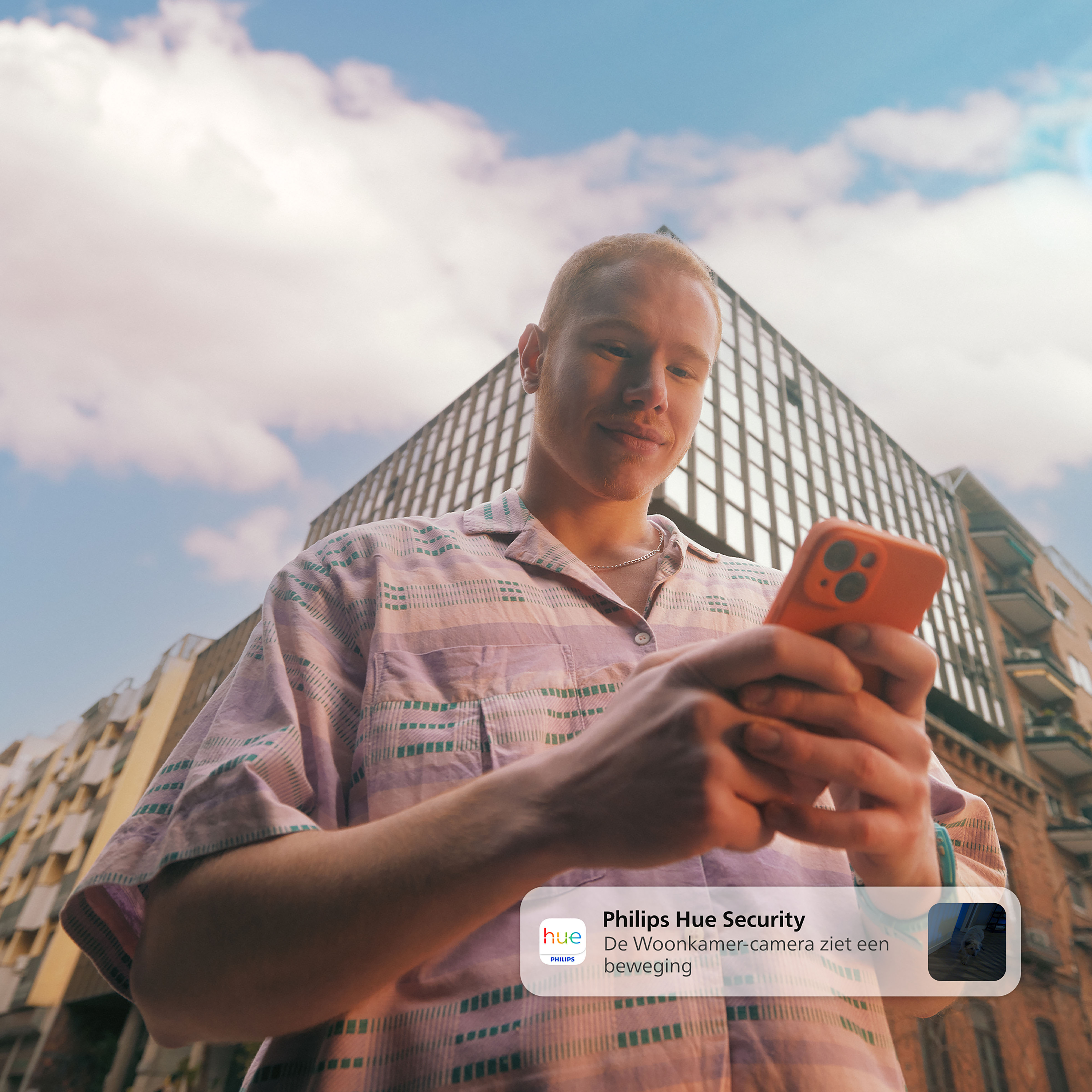 Mann mit orangefarbenem Telefon, Blick in die Kamera, Stadtbild im Hintergrund.