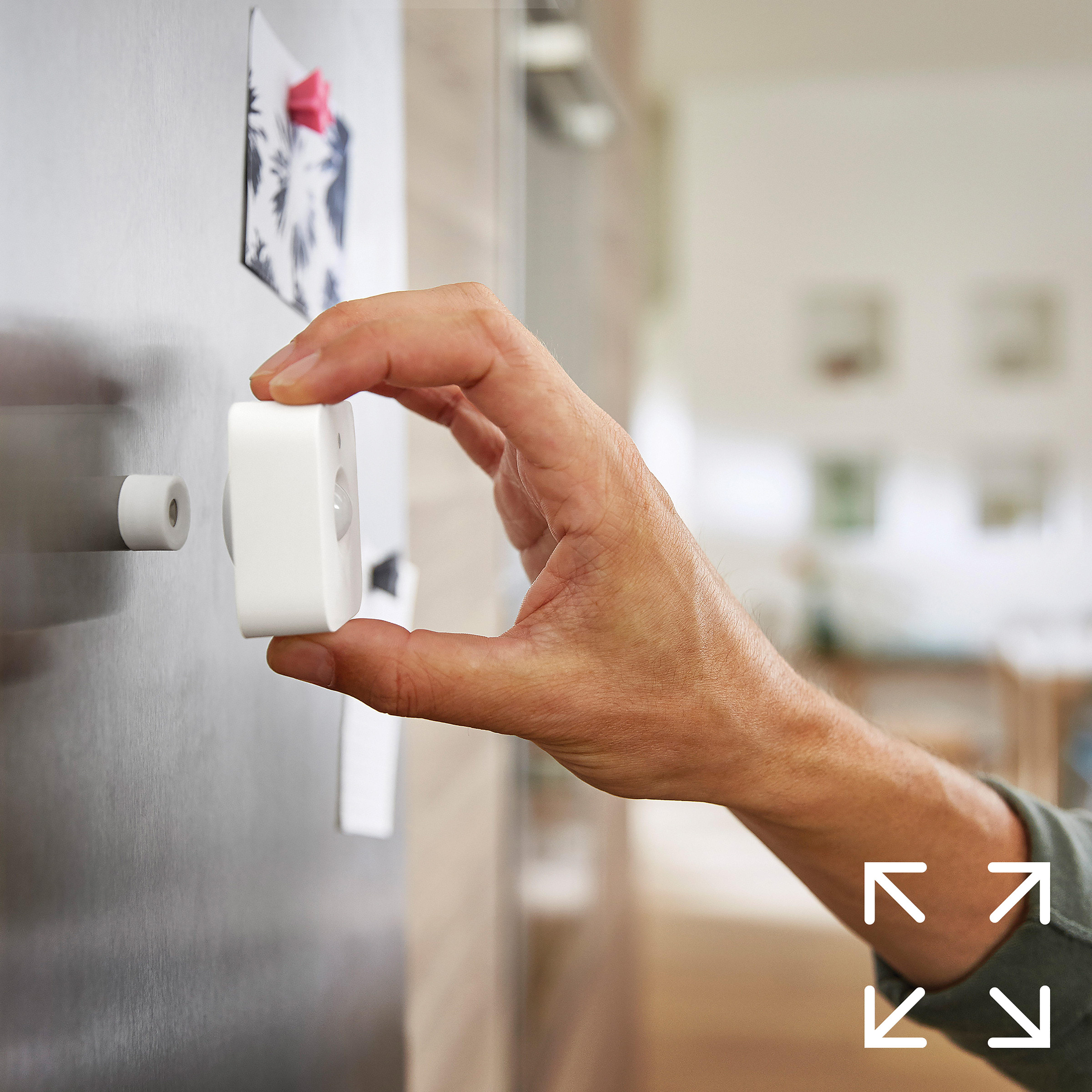 Ręka mocująca biały czujnik inteligentnego domu do lodówki.