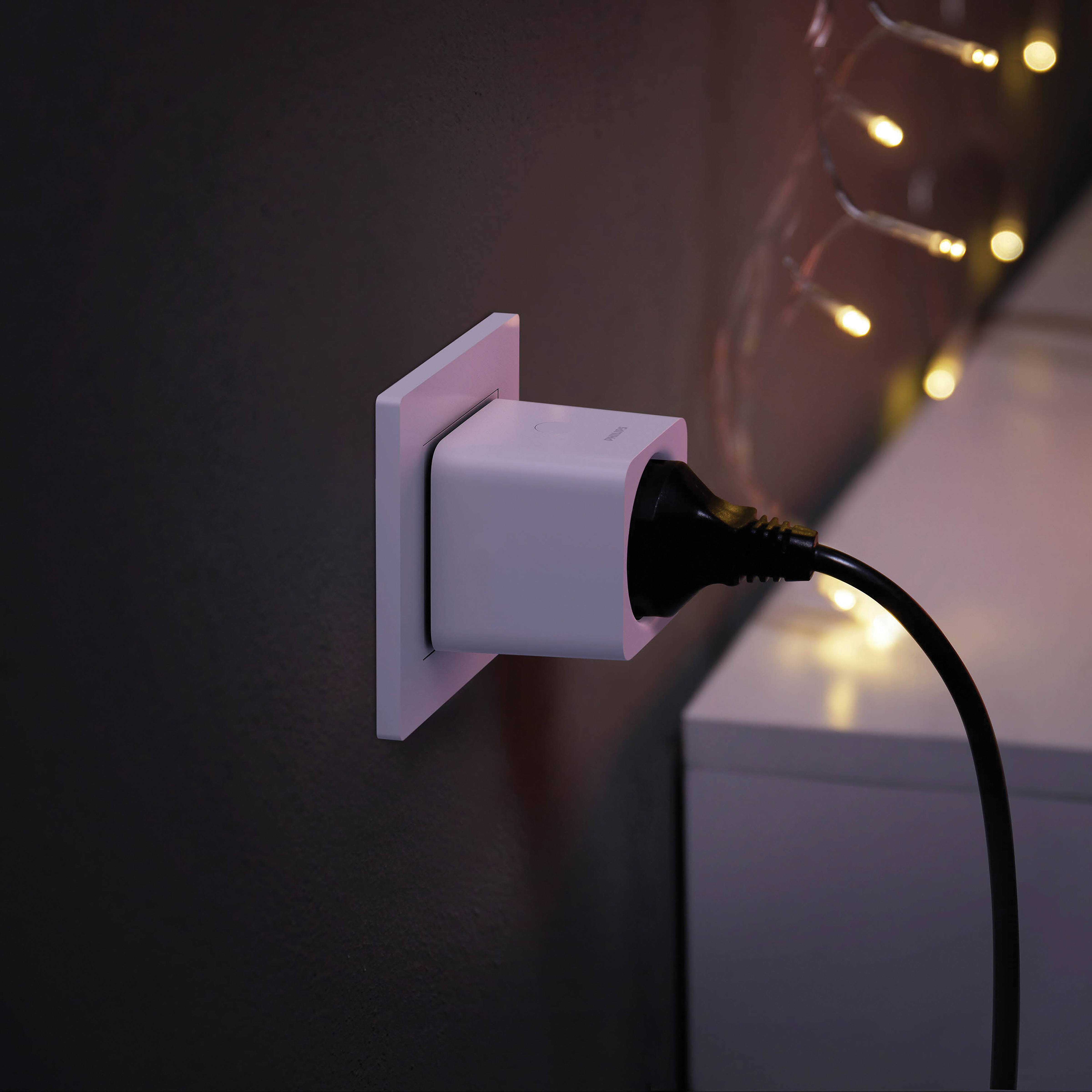 Weißer Smart Plug in der Steckdose. Schwarzes Kabel und Lichterkette sichtbar.