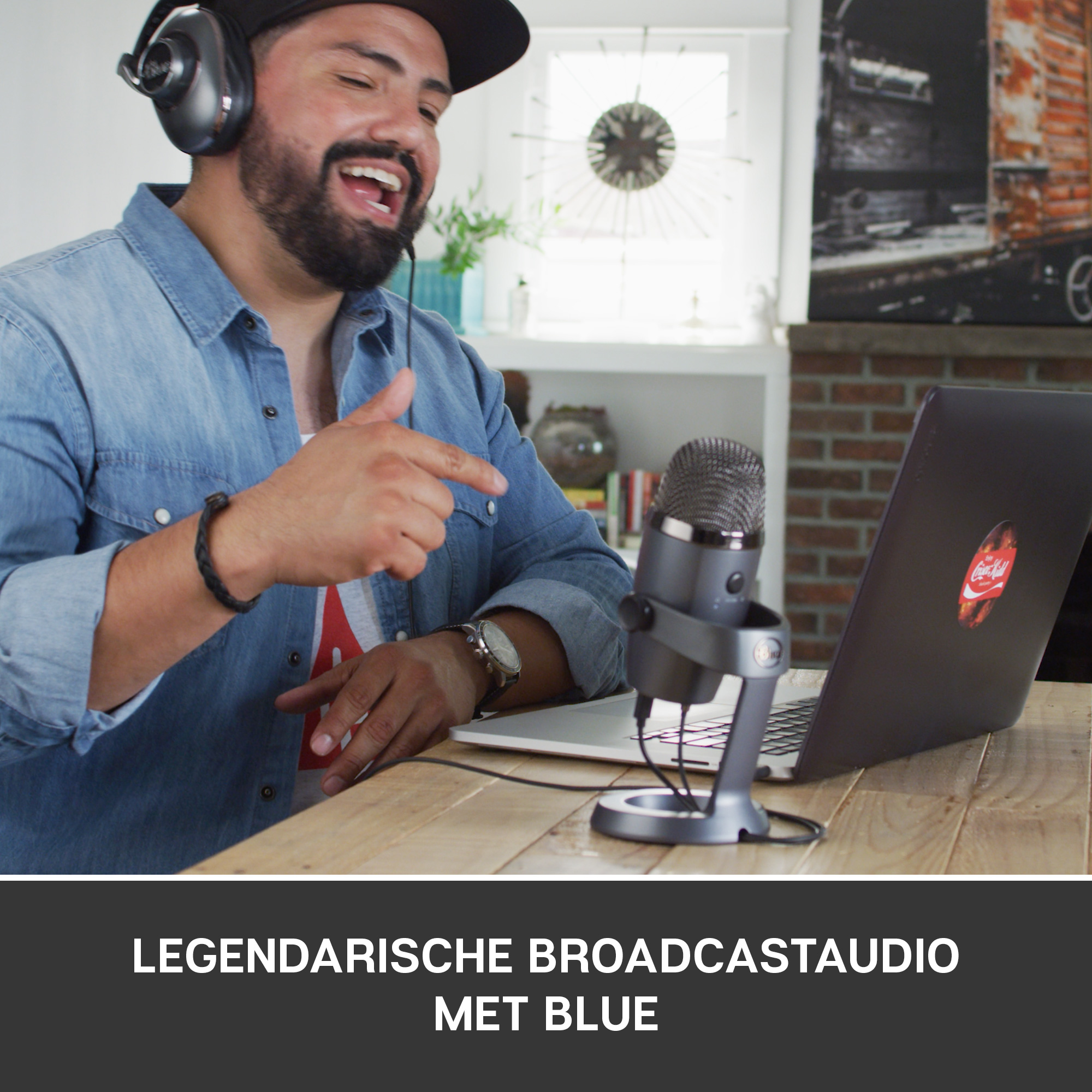 Mann mit Kopfhörern singt in Mikrofon. Laptop mit Coca-Cola Aufkleber. Holztisch.