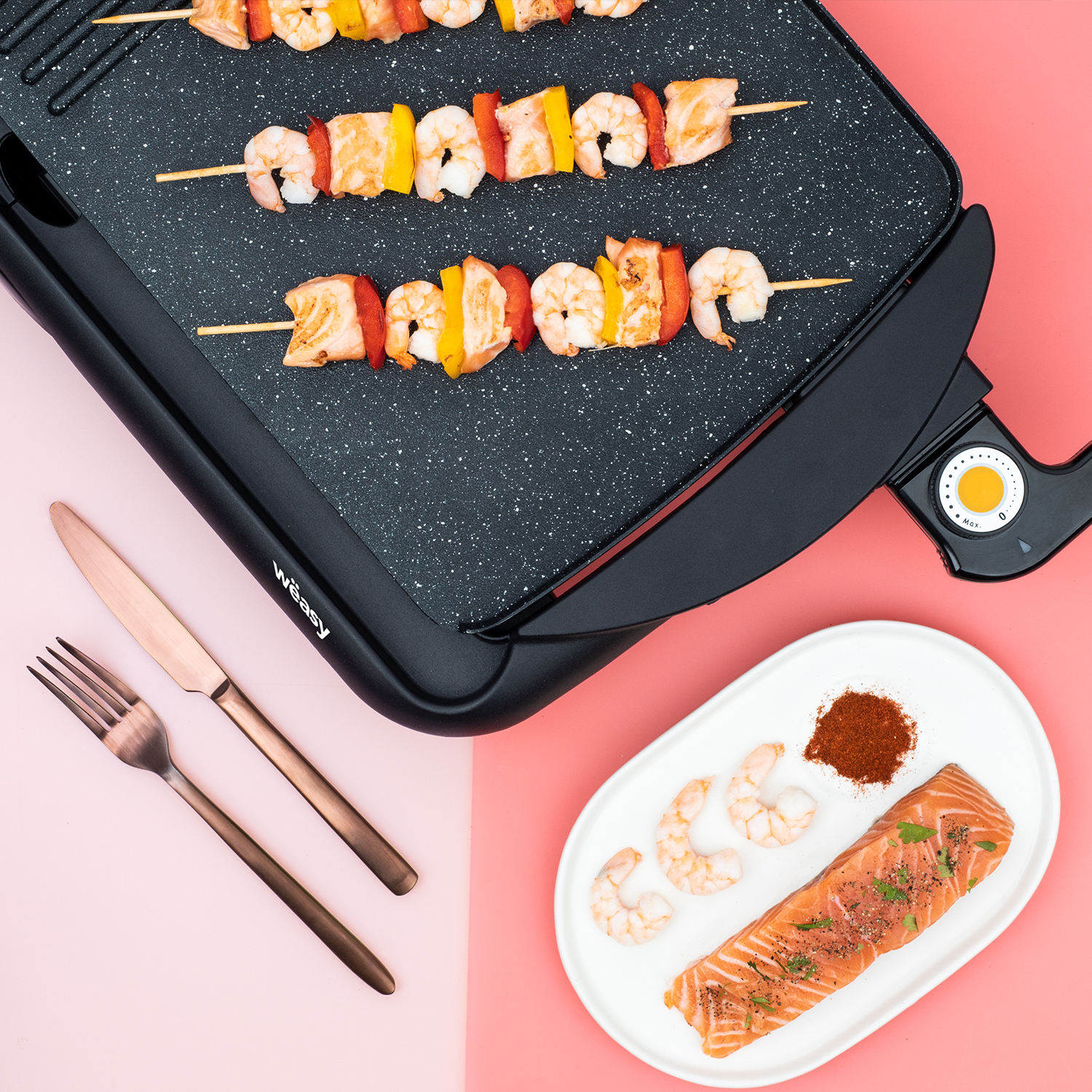 Grill mit Spießen, Lachs und Garnelen auf rosa und schwarzer Oberfläche.
