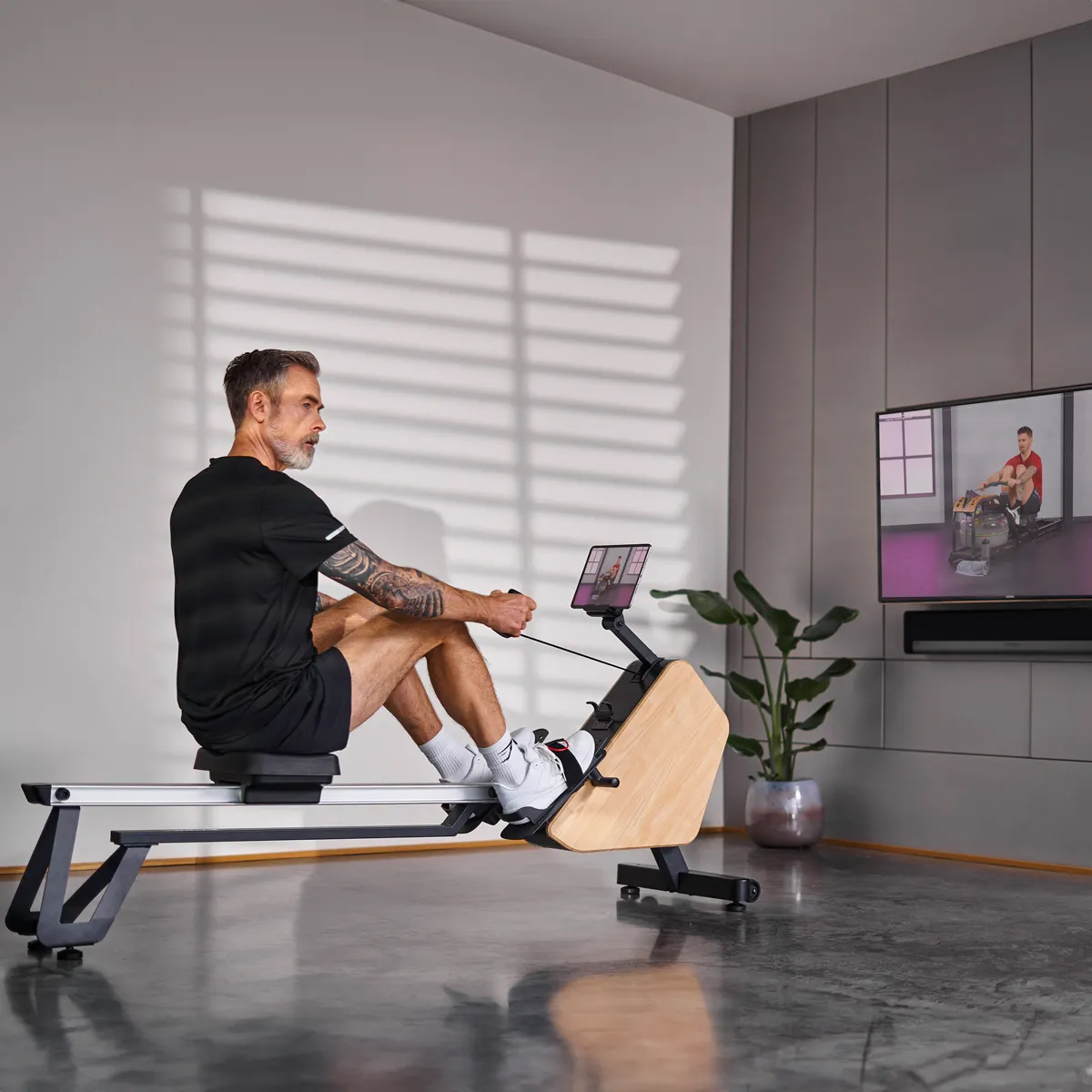 Mann auf Rudermaschine, mit TV, der gleiche Aktivität zeigt. Innenraum.