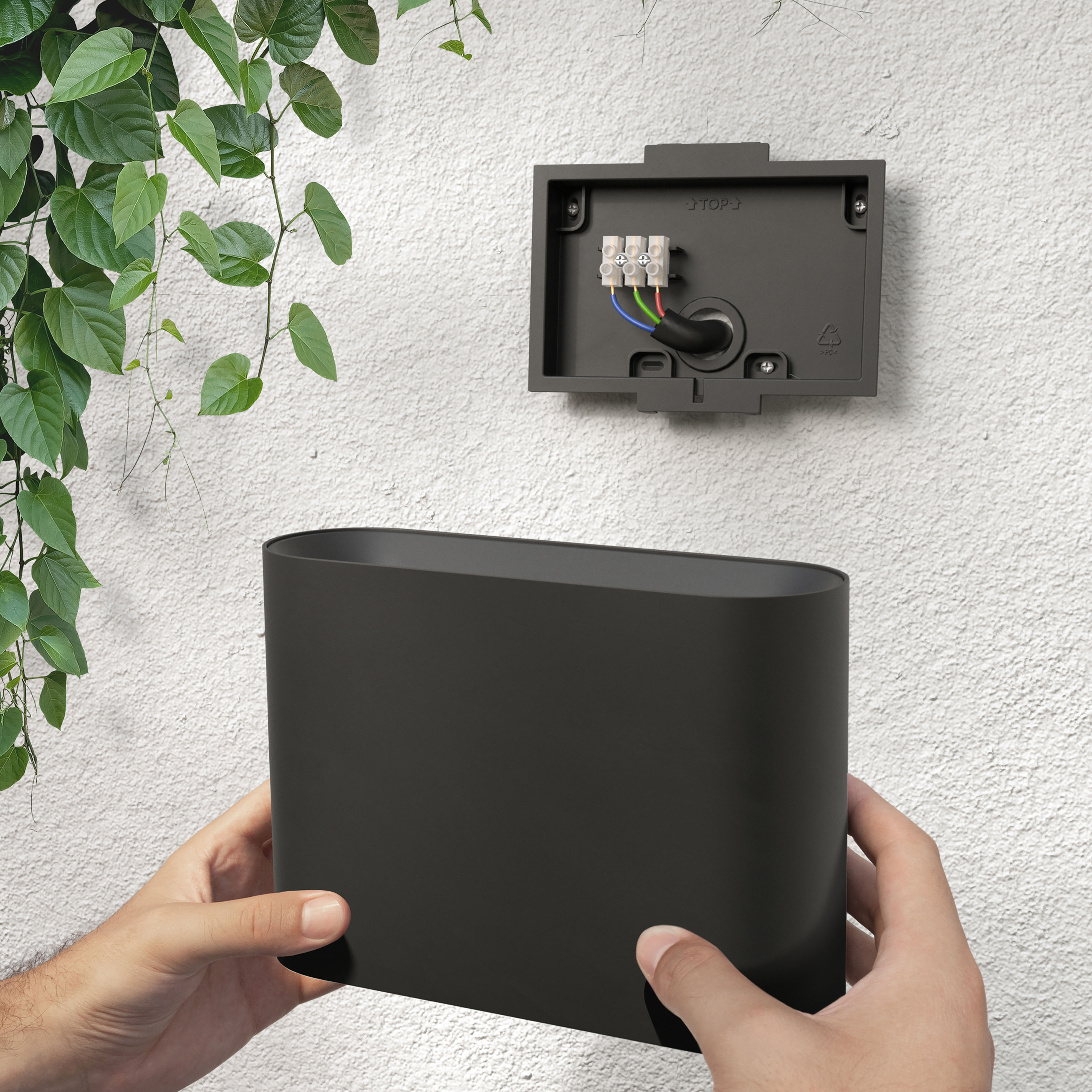 Hände installieren eine schwarze Außenwandleuchte an einer weißen Stuckwand.