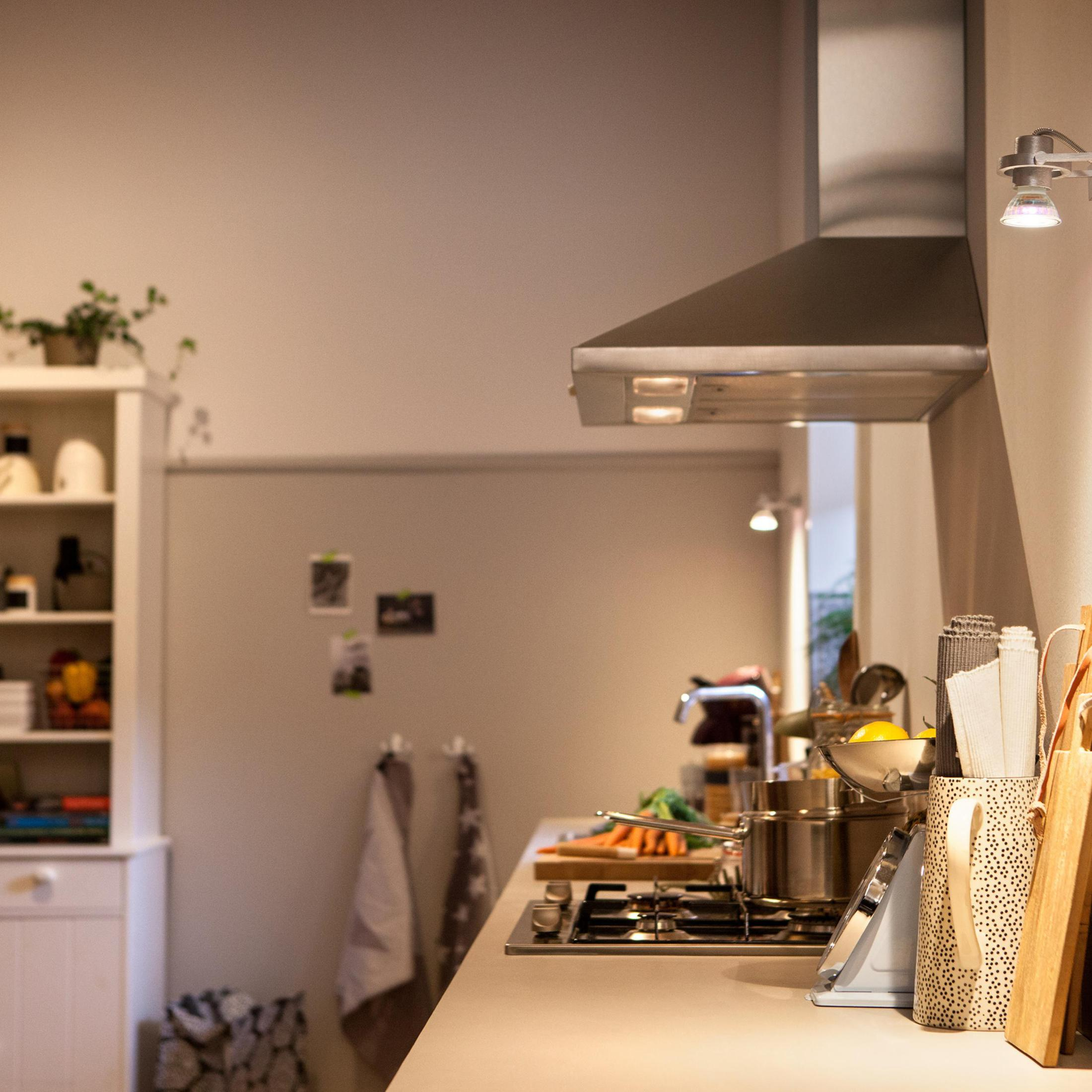 Une cuisine avec une cuisinière, des légumes et une hotte aspirante en inox. Une lumière allumée.