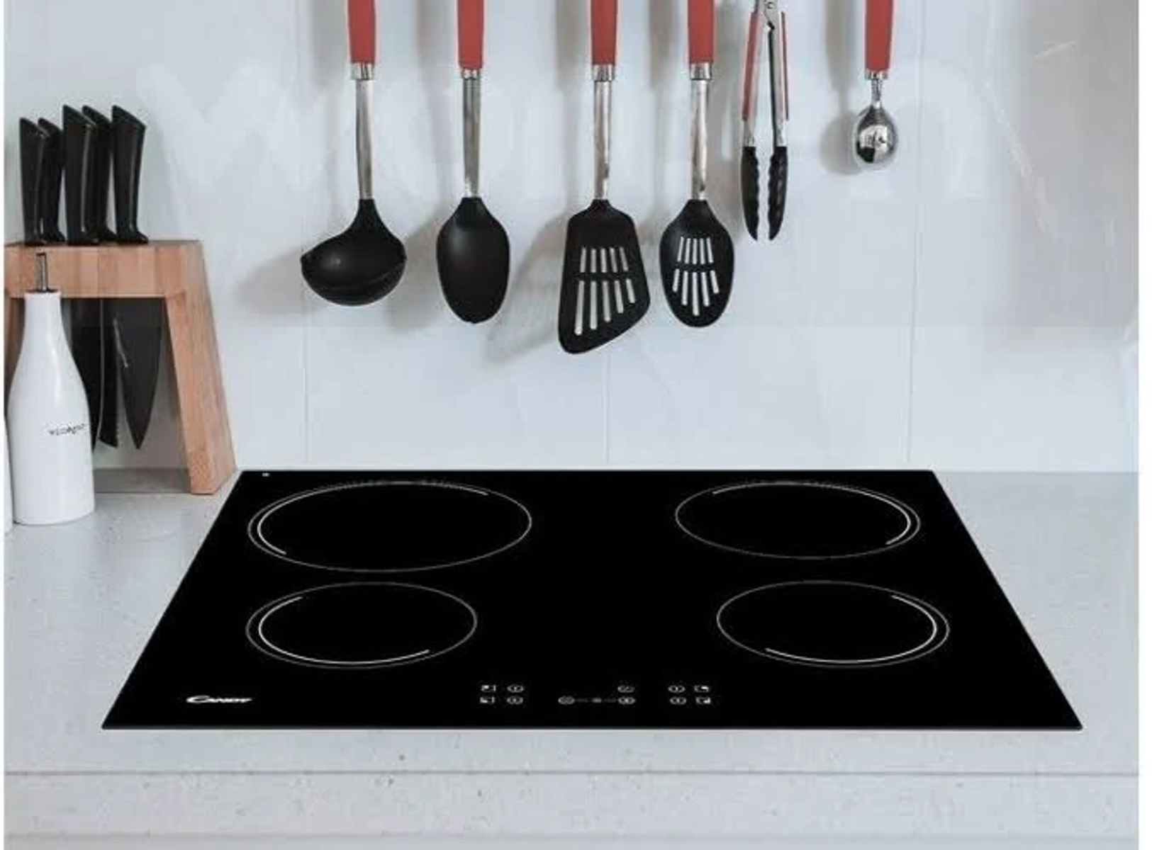 Czarna płyta indukcyjna z czterema okrągłymi palnikami, wiszące przybory kuchenne.