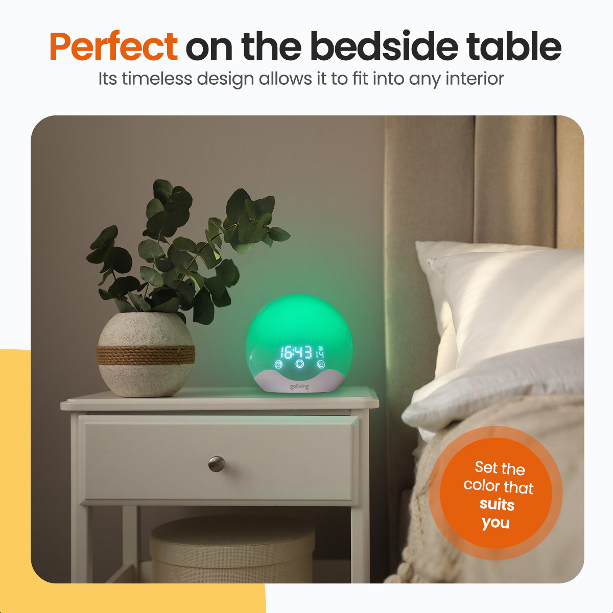 Green light-emitting bedside lamp next to a white nightstand with plant and a bed with a pillow.