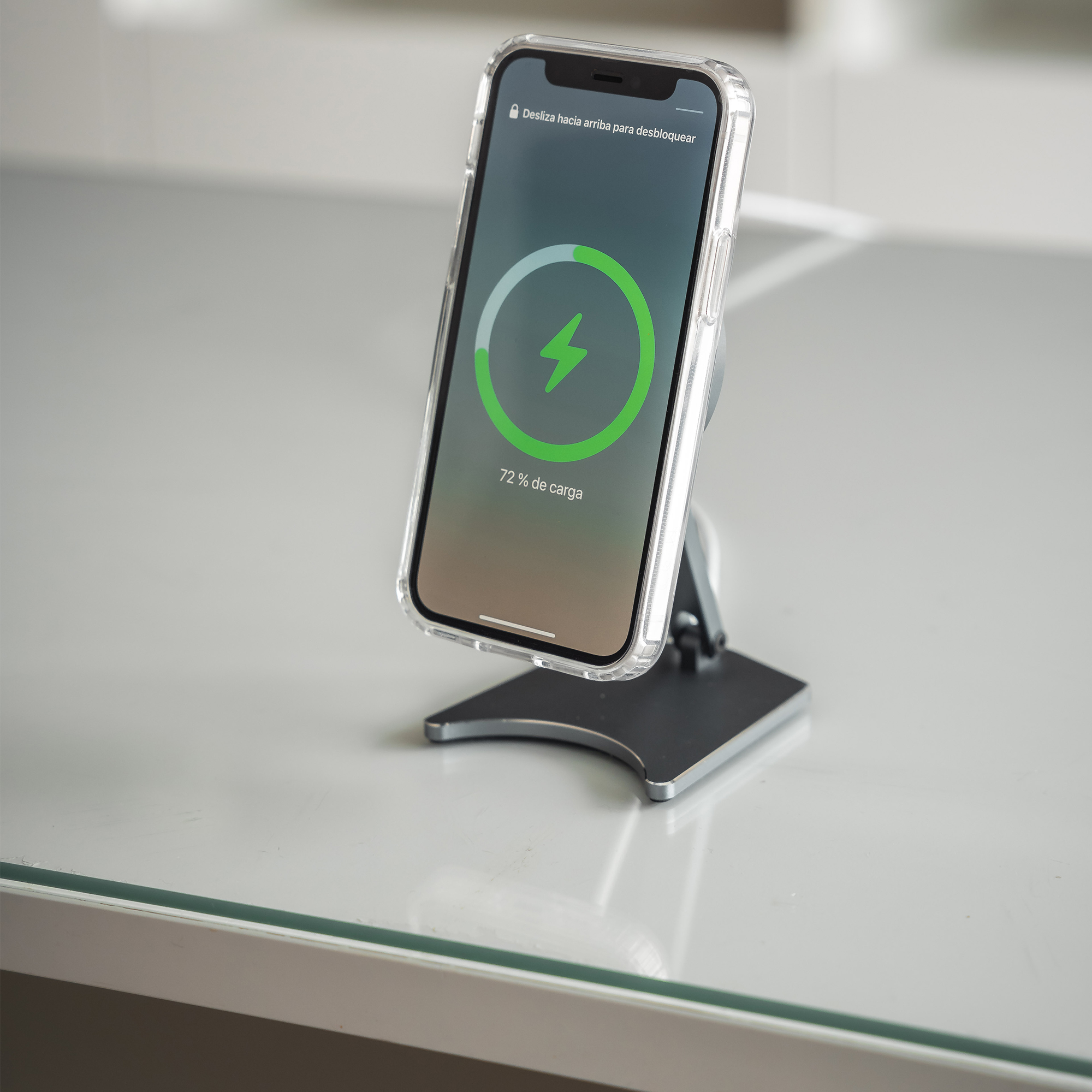 Smartphone cargando en un soporte. La pantalla muestra un icono de carga y 72% de carga. Mesa blanca.