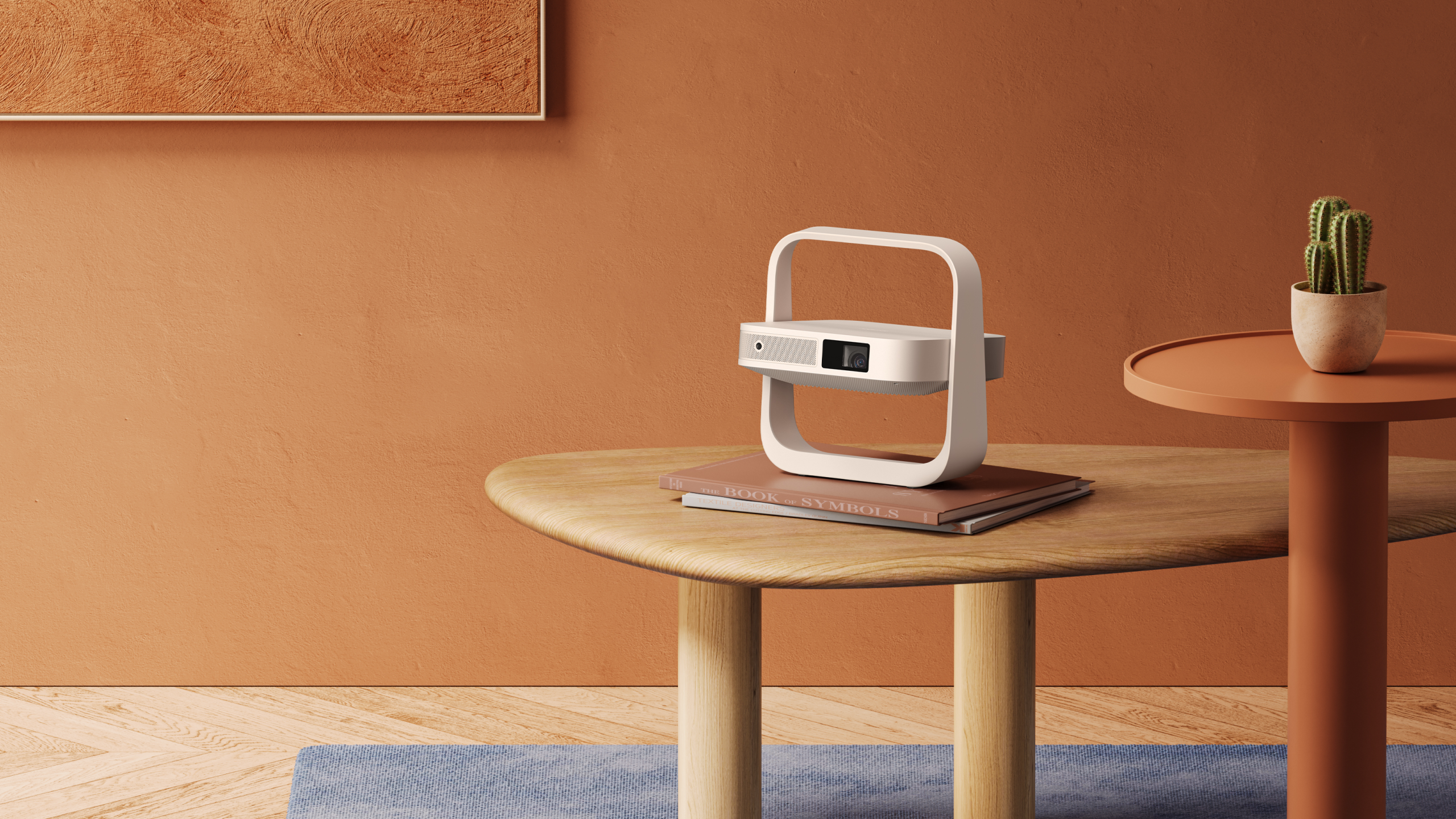 Projektor na stole z książkami i małym kaktusem oraz pomarańczową ścianą.