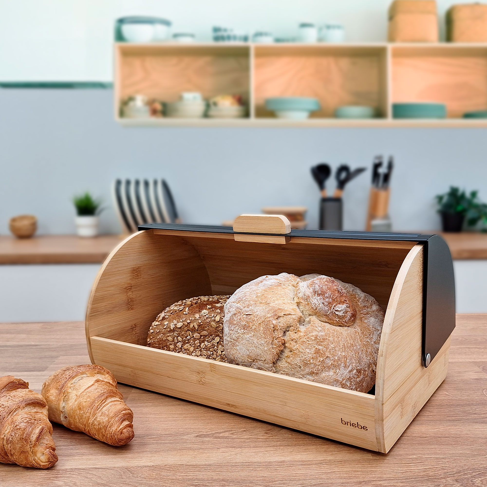 Caja de pan de madera con pan dentro, cruasanes delante, fondo de cocina.