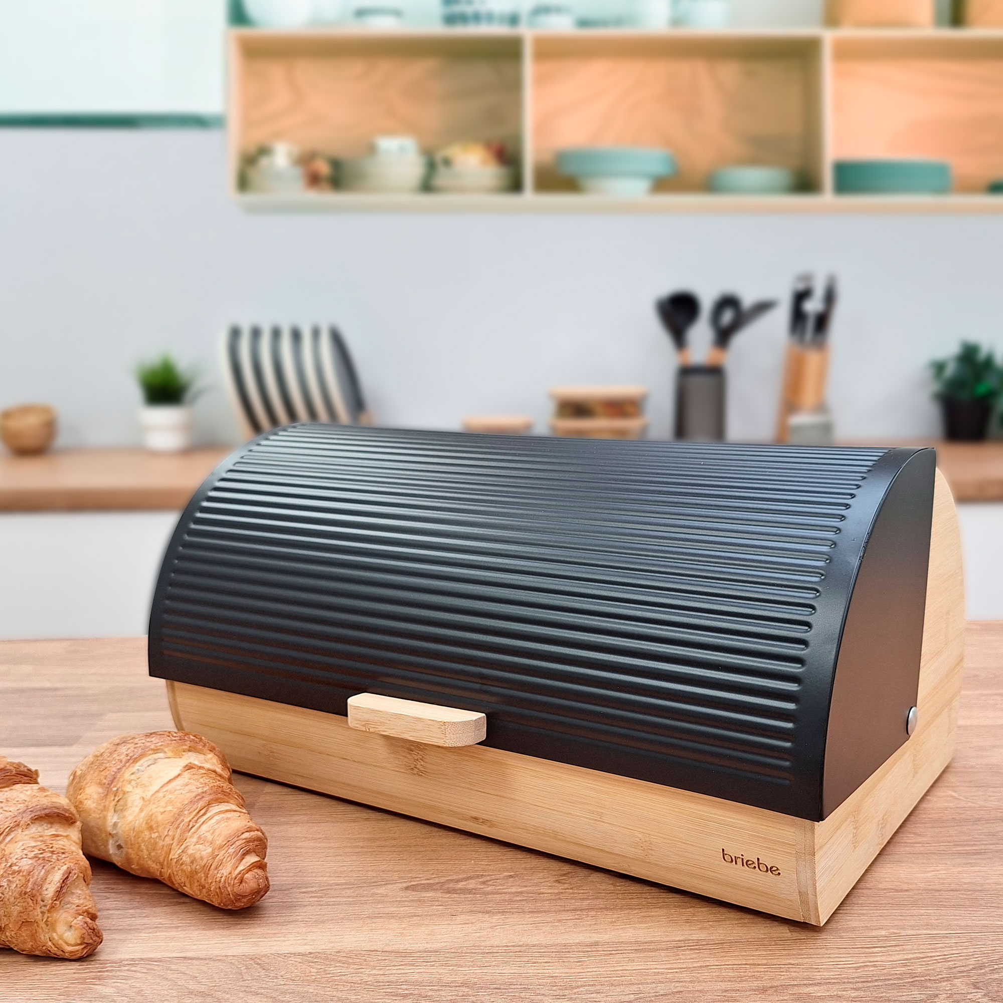 Panera de madera con tapa negra, sobre mesa de madera con cruasanes en primer plano.