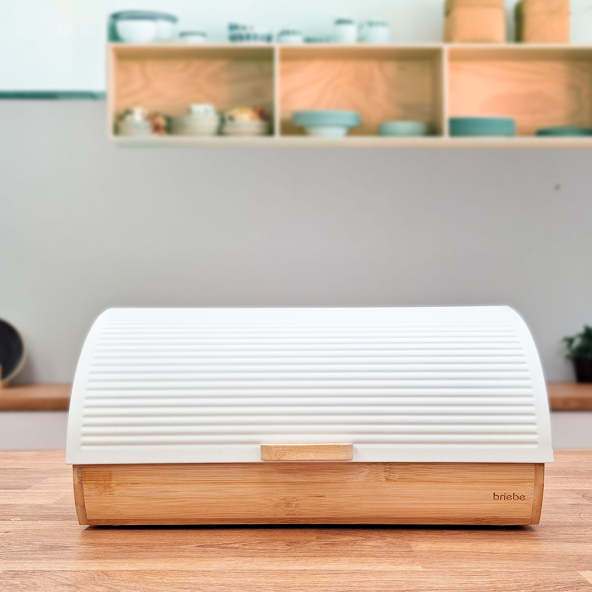 Panera blanca con base y asa de madera, colocada sobre una mesa de madera, contra un fondo de cocina.