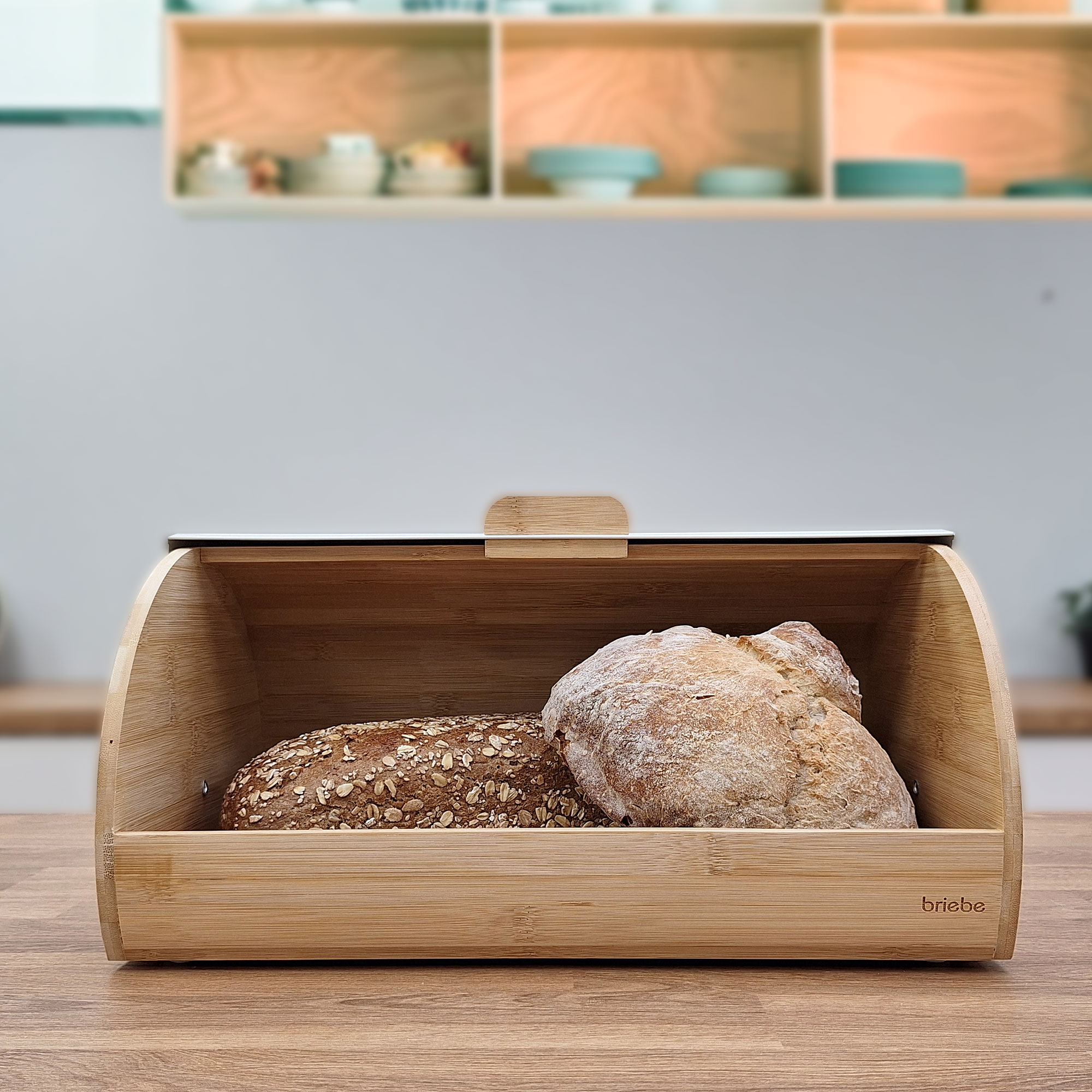 Una panera de madera con dos hogazas de pan dentro, sobre una mesa de madera.