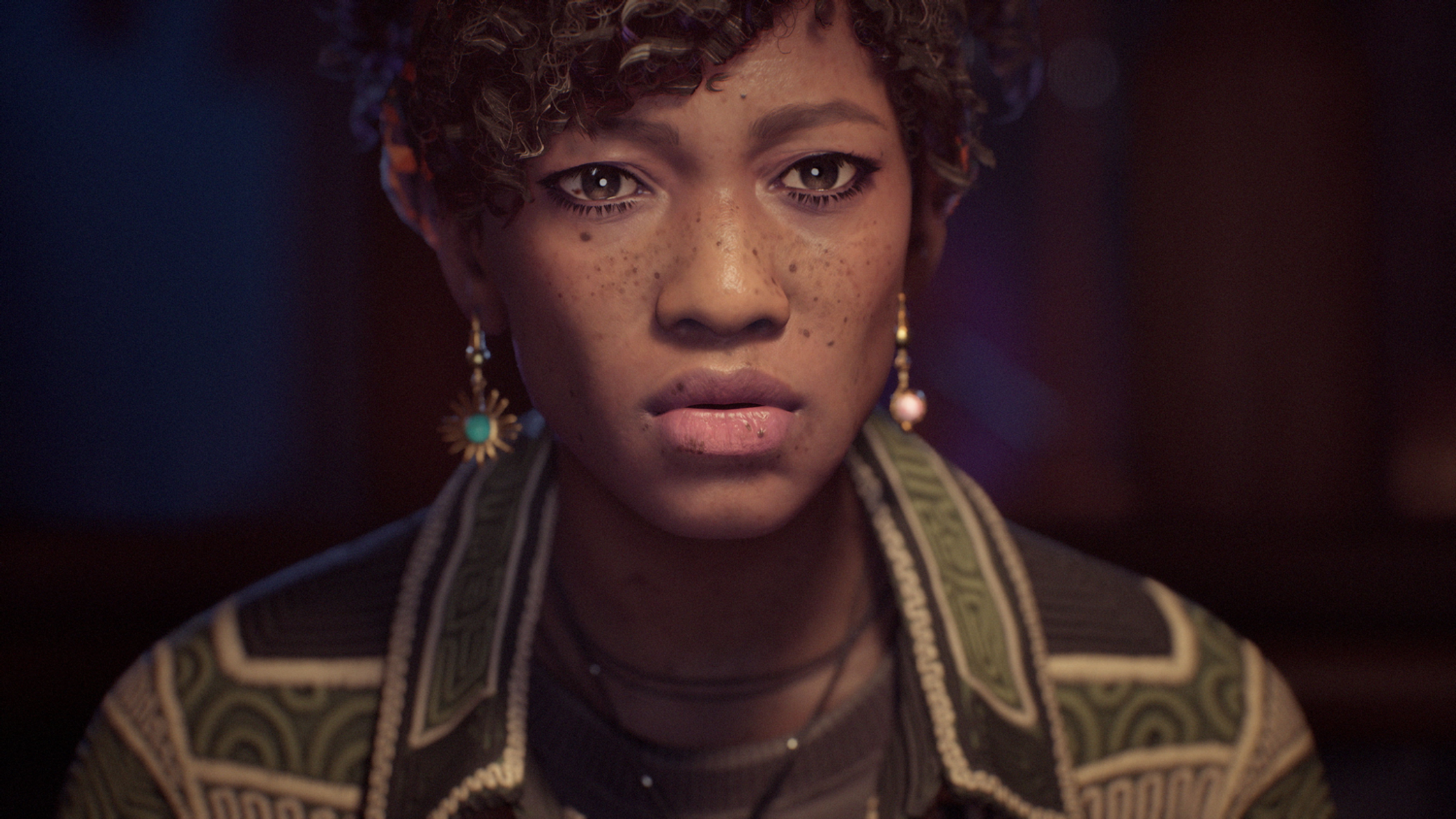 Kobieta z kręconymi włosami, w kurtce i kolczykach. Patrzy prosto na widza.