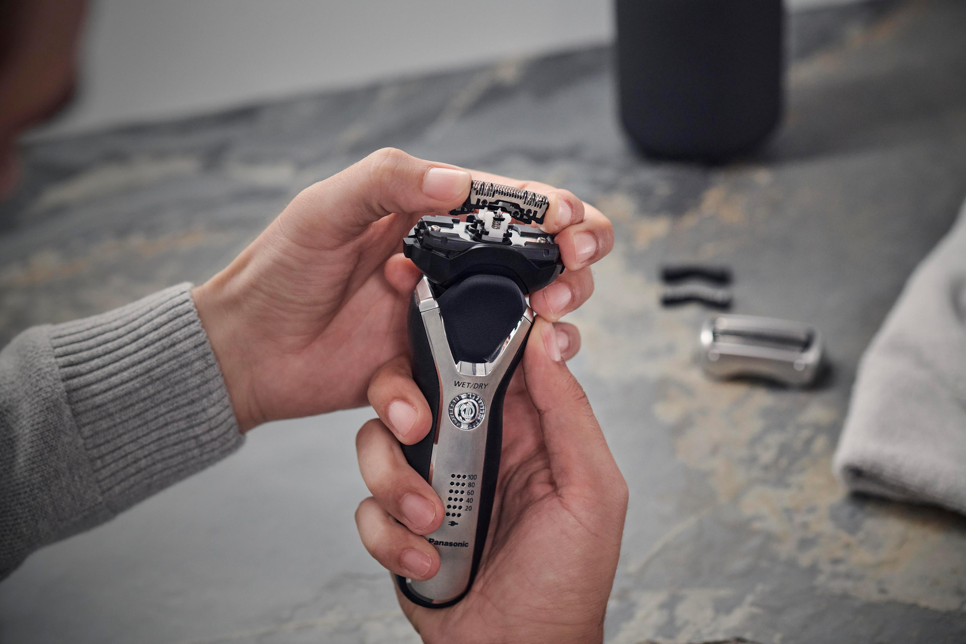 Dłonie trzymają srebrno-czarną golarkę elektryczną, pokazując głowicę golącą i jej elementy.