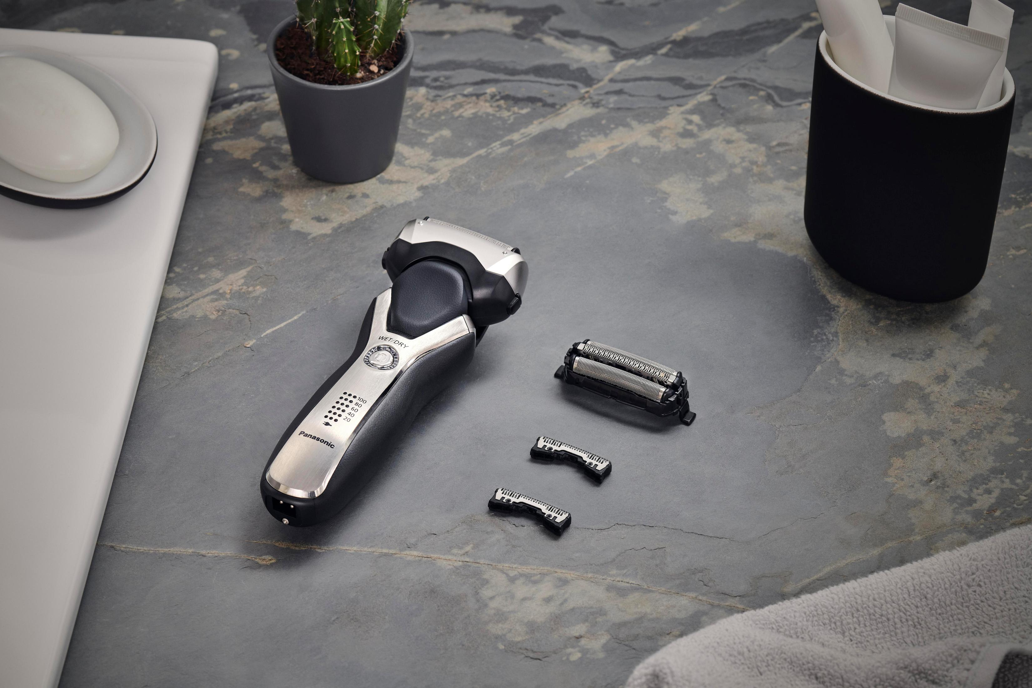 Golarka elektryczna z akcesoriami, umieszczona na powierzchni przypominającej kamień.