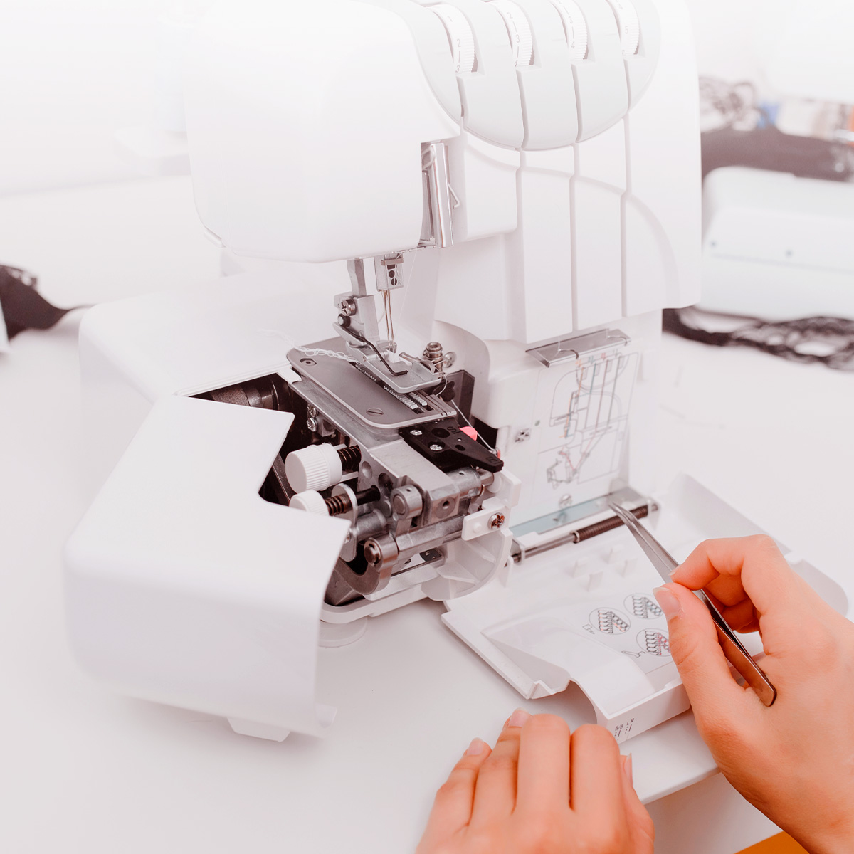 Una máquina de coser overlock blanca, con las manos de una persona cerca del área de la aguja y carretes de hilo.
